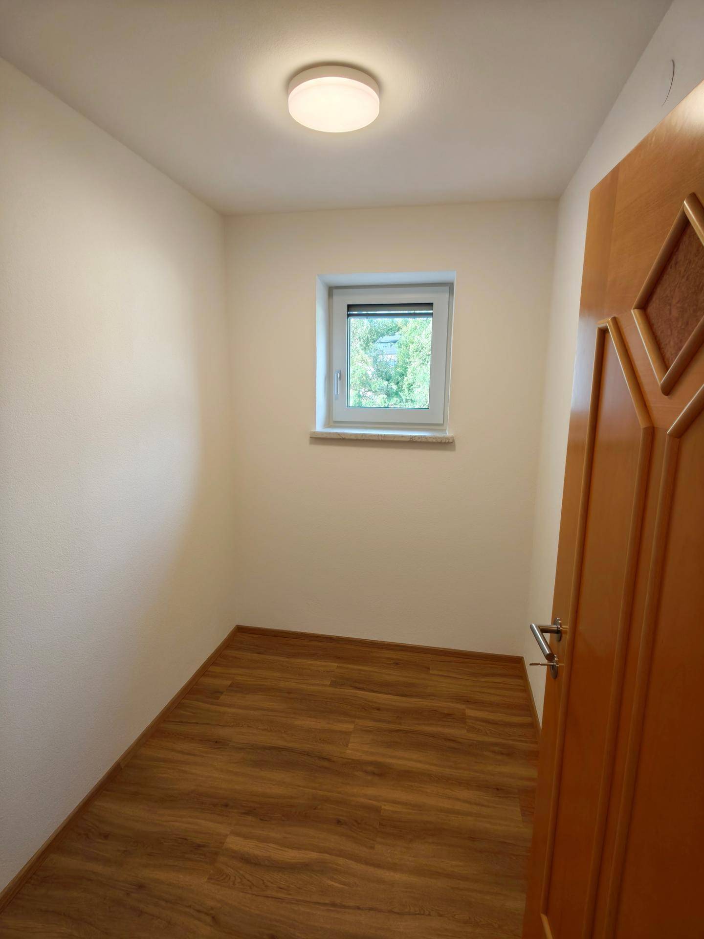 Kleiner heller Raum mit Laminatboden und Fenster, ideal als Abstellraum oder Büro.