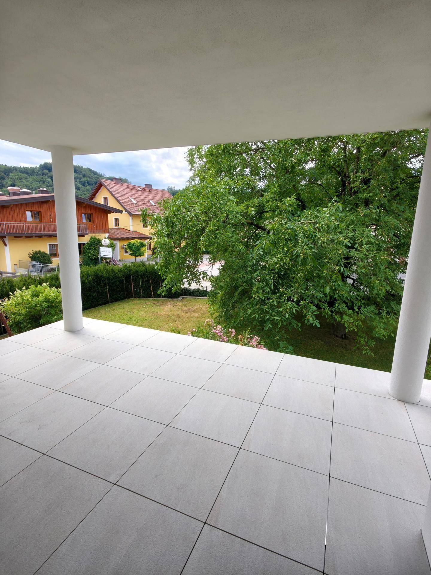 Geräumige überdachte Terrasse mit Fliesenboden und weitem Blick ins Grüne.