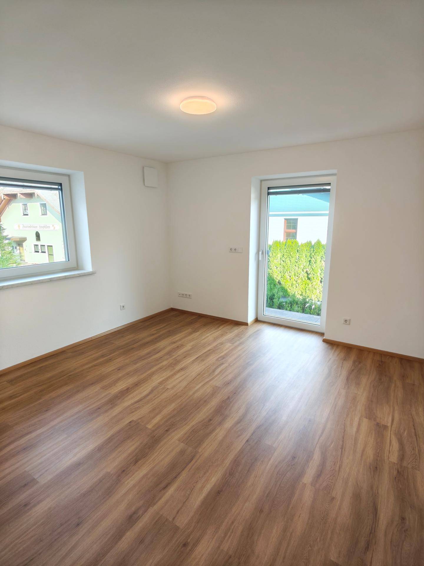 Helles Schlafzimmer mit Laminatboden, Fenster und Zugang zu einem Außenbereich.