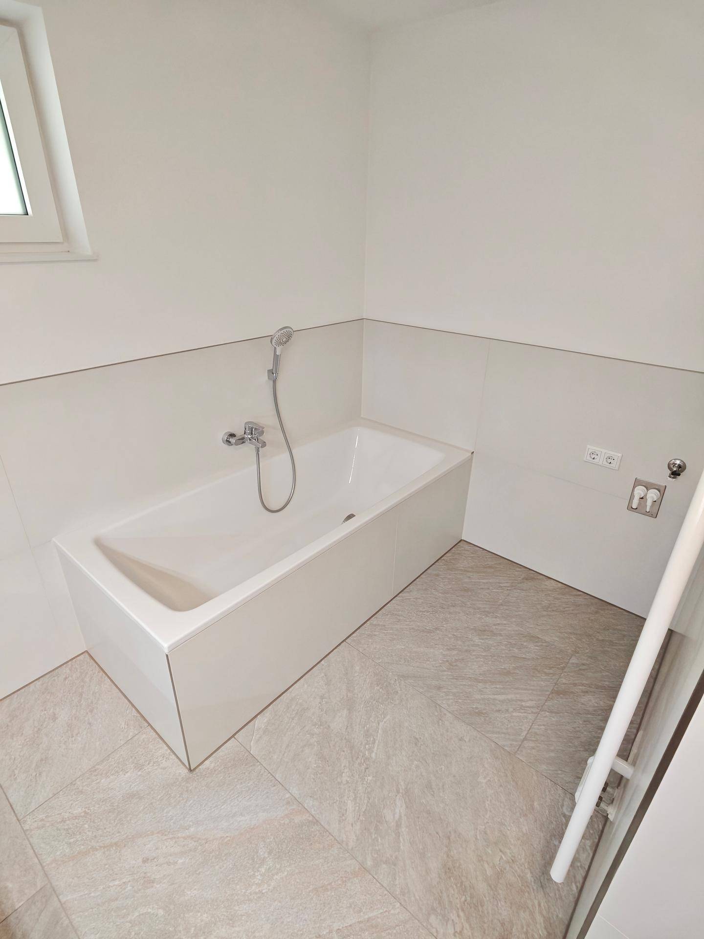 Helle Badewanne mit Duschfunktion und beheiztem Handtuchhalter in einem modernen Badezimmer.