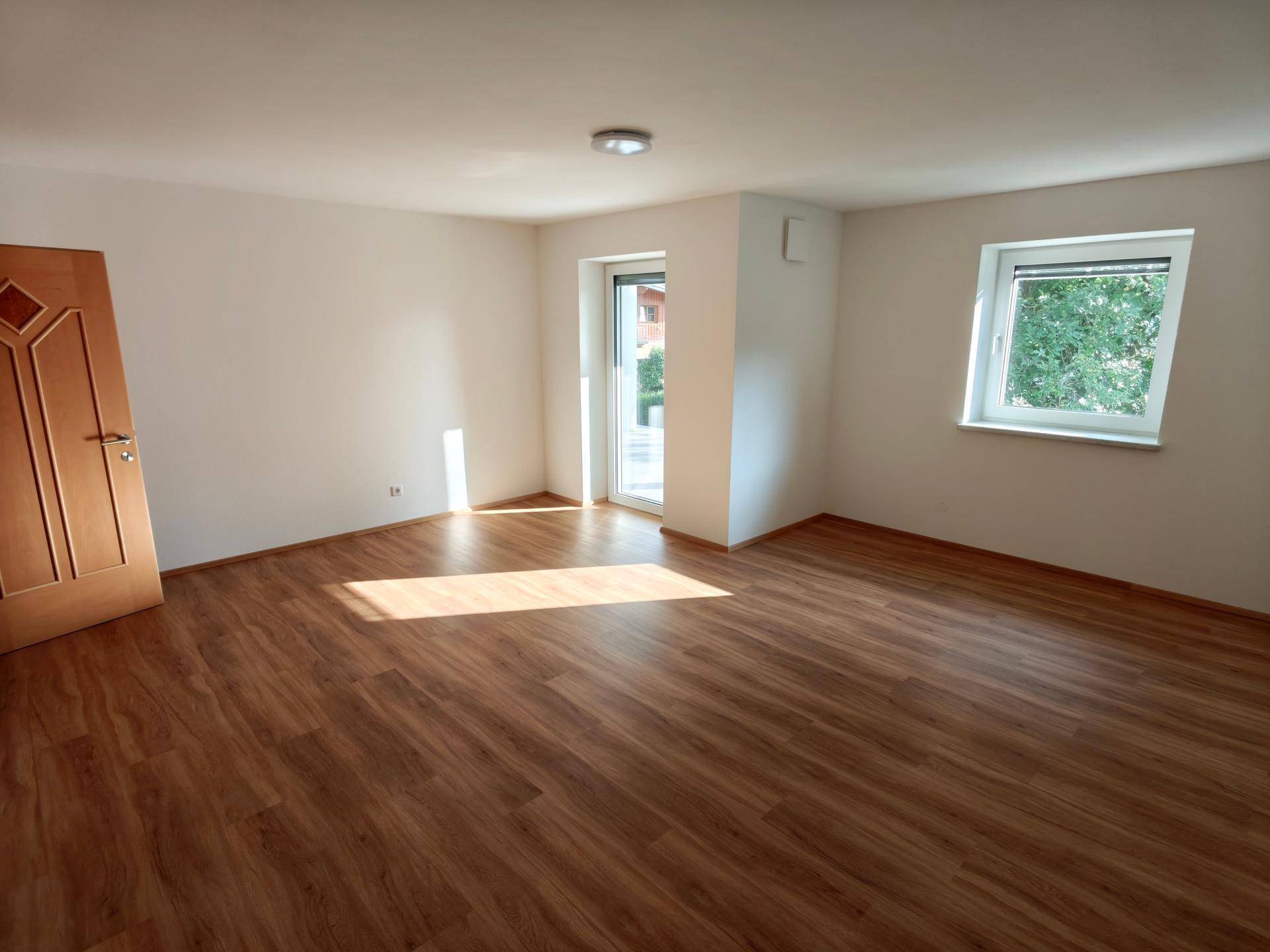Helles Schlafzimmer mit Laminatboden, Fenster und Zugang zu einem Außenbereich.