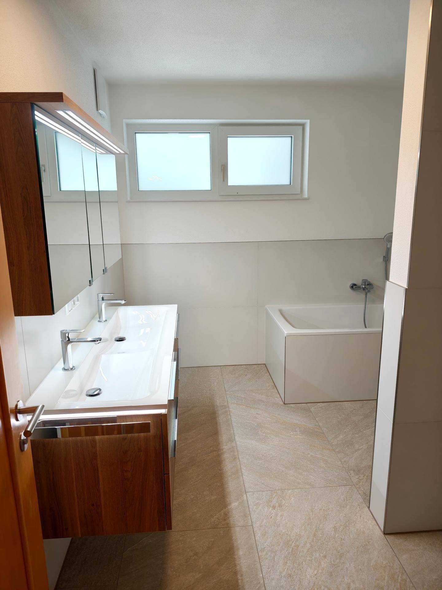 Helles Badezimmer mit Fenster, Doppelwaschbecken und integrierter Badewanne.