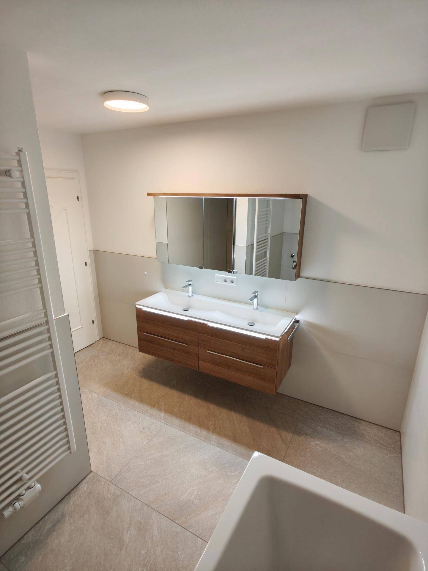 Modernes Badezimmer mit Doppelwaschbecken, Holzunterschrank und beheiztem Handtuchhalter.