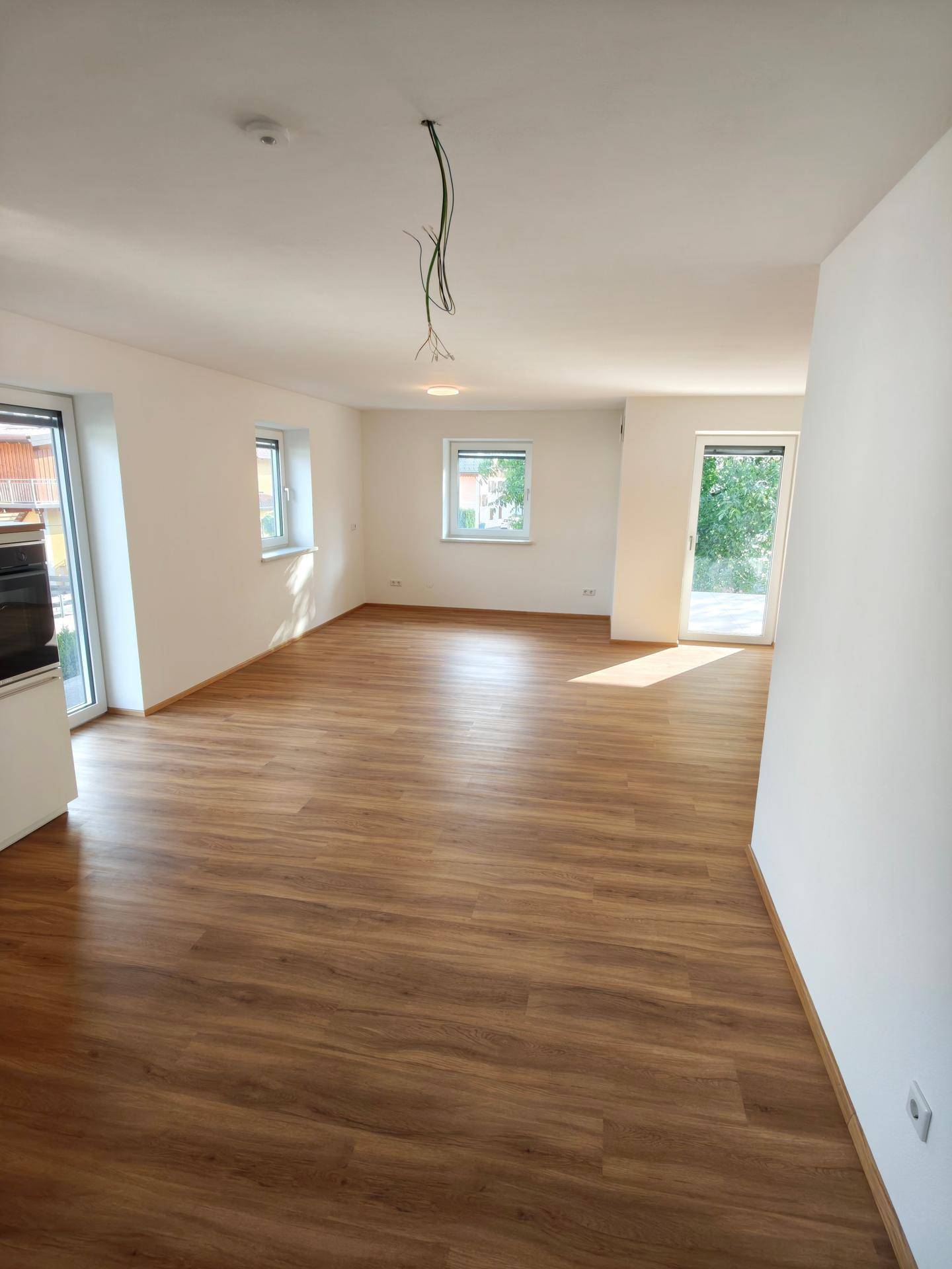 Heller Wohnraum mit Laminatboden, mehreren Fenstern und viel Tageslicht.