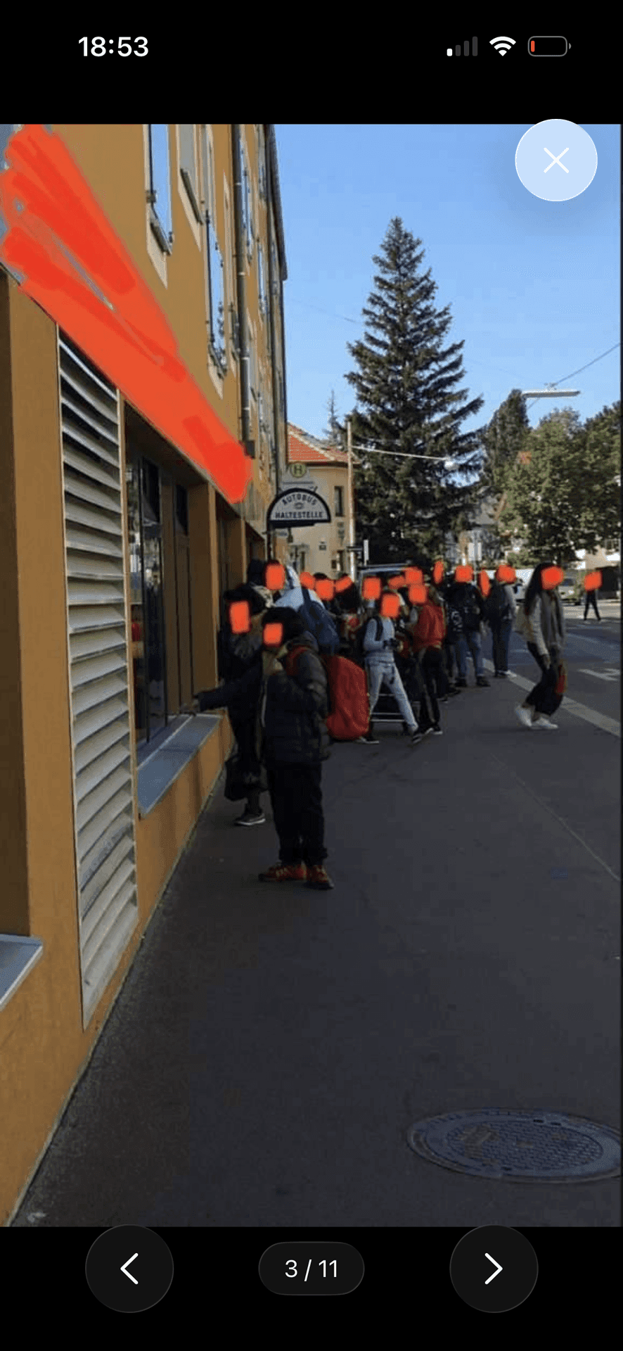 Fassade eines Gebäudes mit einer Schlange von Menschen auf dem Bürgersteig vor einem Geschäft.
