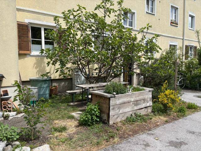 Kleiner Gartenbereich mit Sitzgelegenheiten und Hochbeet vor dem Gebäude.