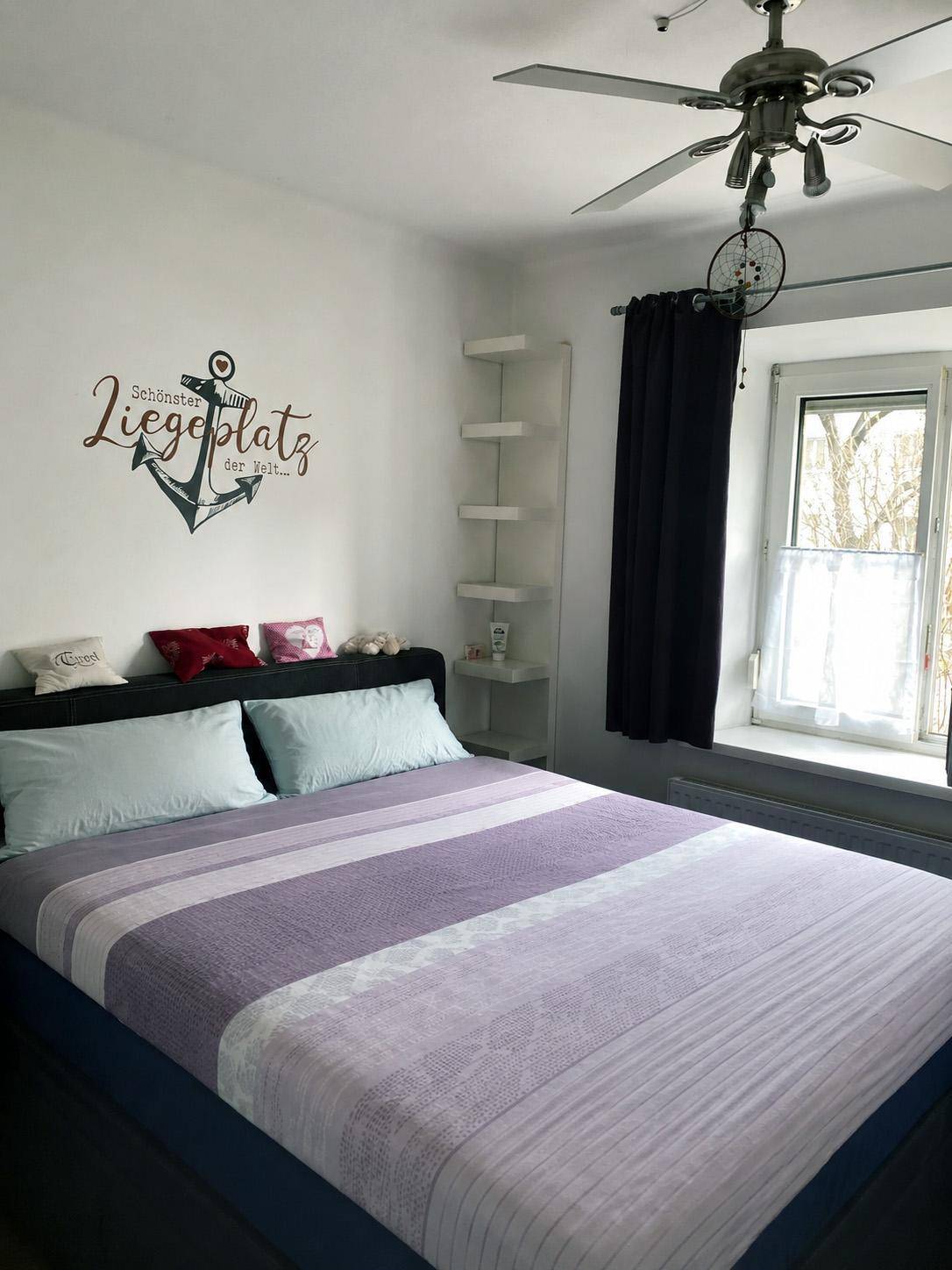 Gemütliches Schlafzimmer mit Doppelbett, Wanddekoration und Deckenventilator.