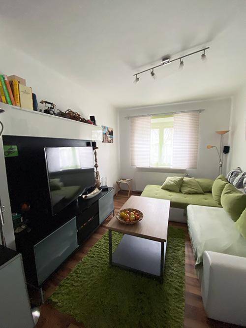Helles Wohnzimmer mit Sofa, Couchtisch und Fernseher.