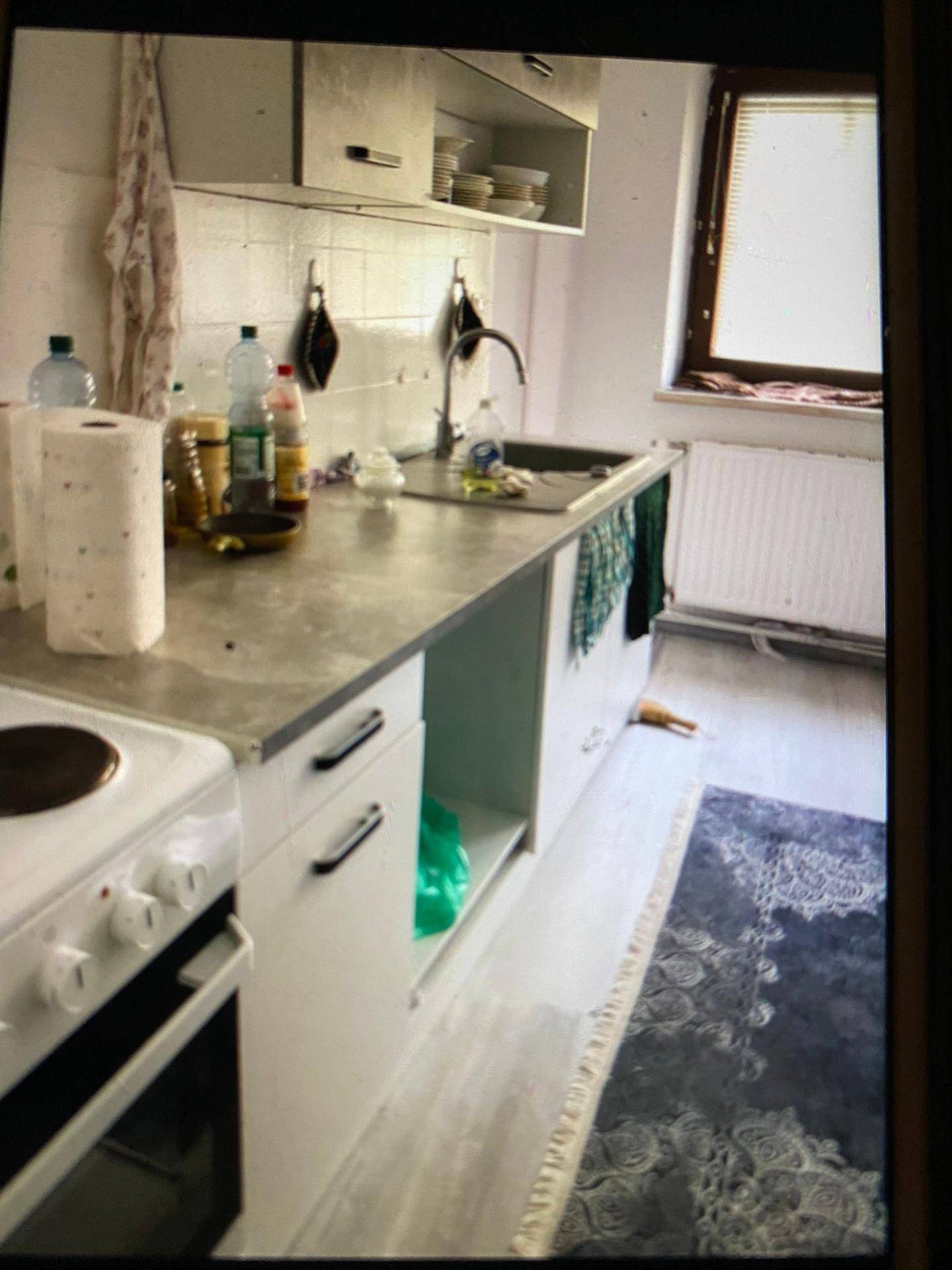 Detailansicht der Küche mit Spüle, Herd und modernen Schränken, daneben ein Fenster.