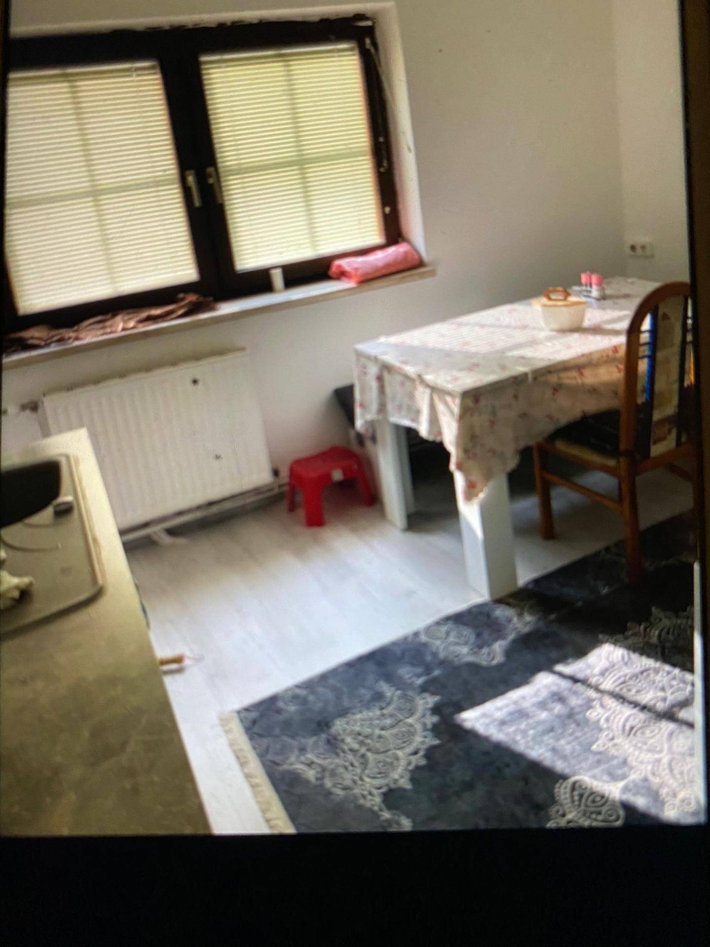 Essbereich mit Tisch und Stuhl, Fenster mit Jalousien und Heizkörper darunter.