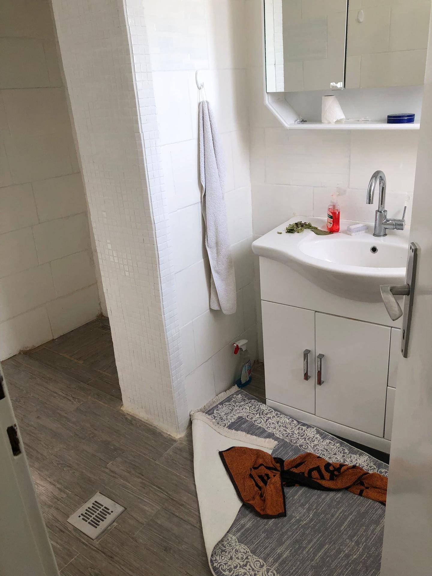 Badezimmer mit Waschbecken, Spiegelschrank und Duschbereich, Wände teilweise gefliest.
