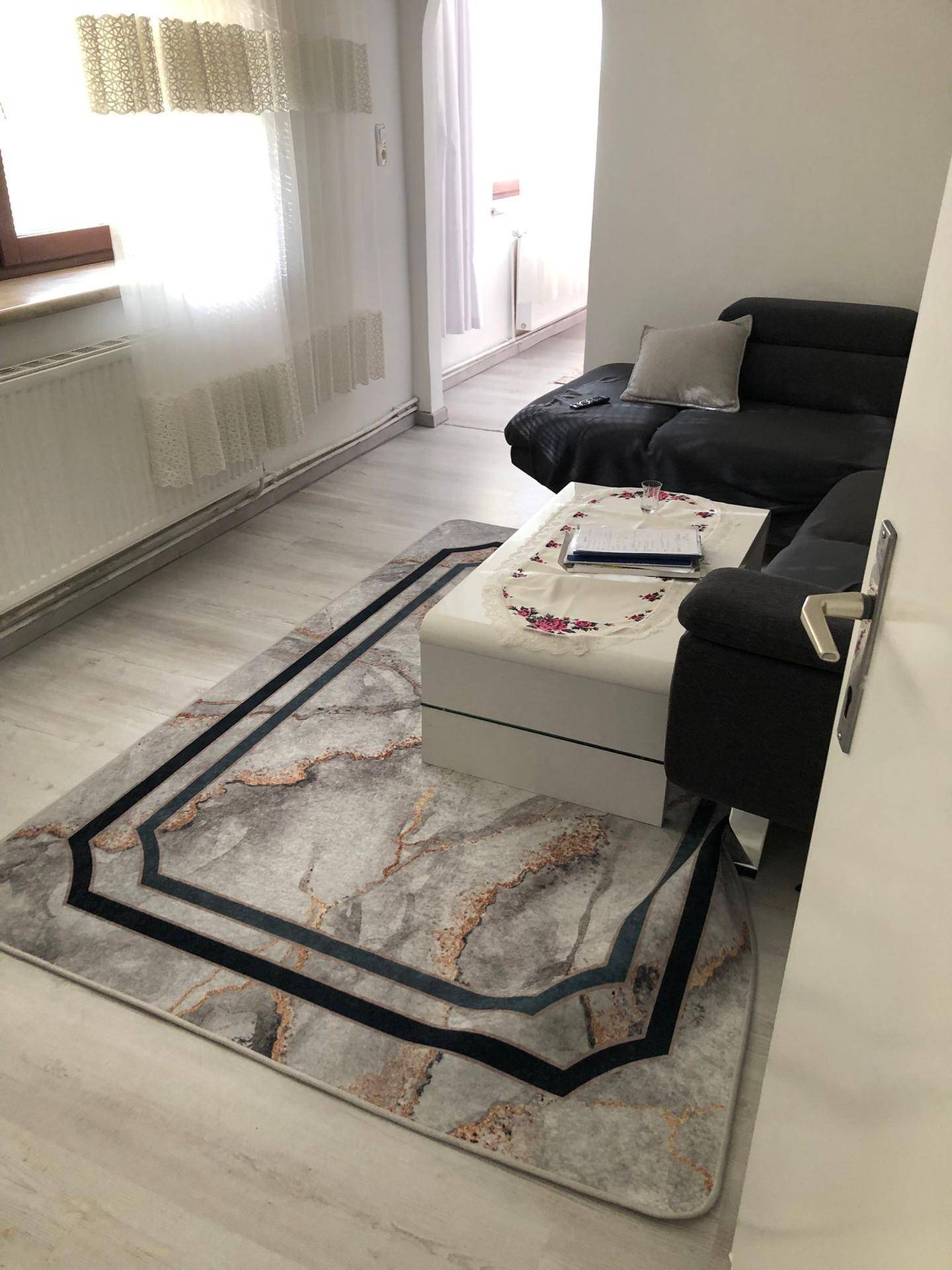 Wohnzimmer mit dunklem Sofa, weißem Couchtisch und gemustertem Teppich, heller Boden.