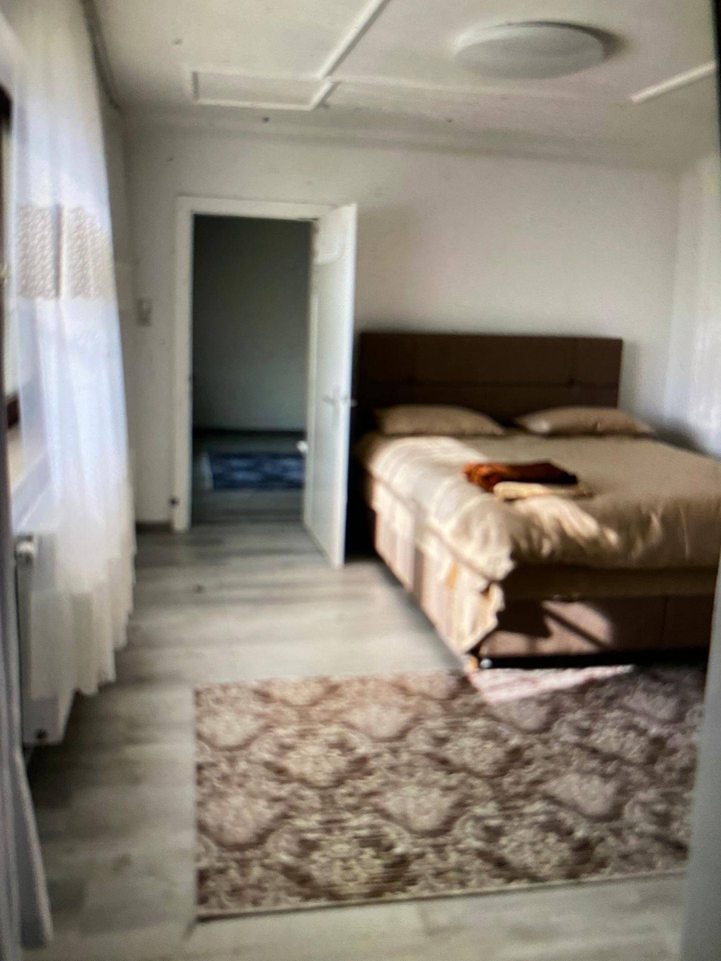 Schlafzimmer mit Doppelbett, Teppich und Fenster mit Vorhängen, heller Laminatboden.