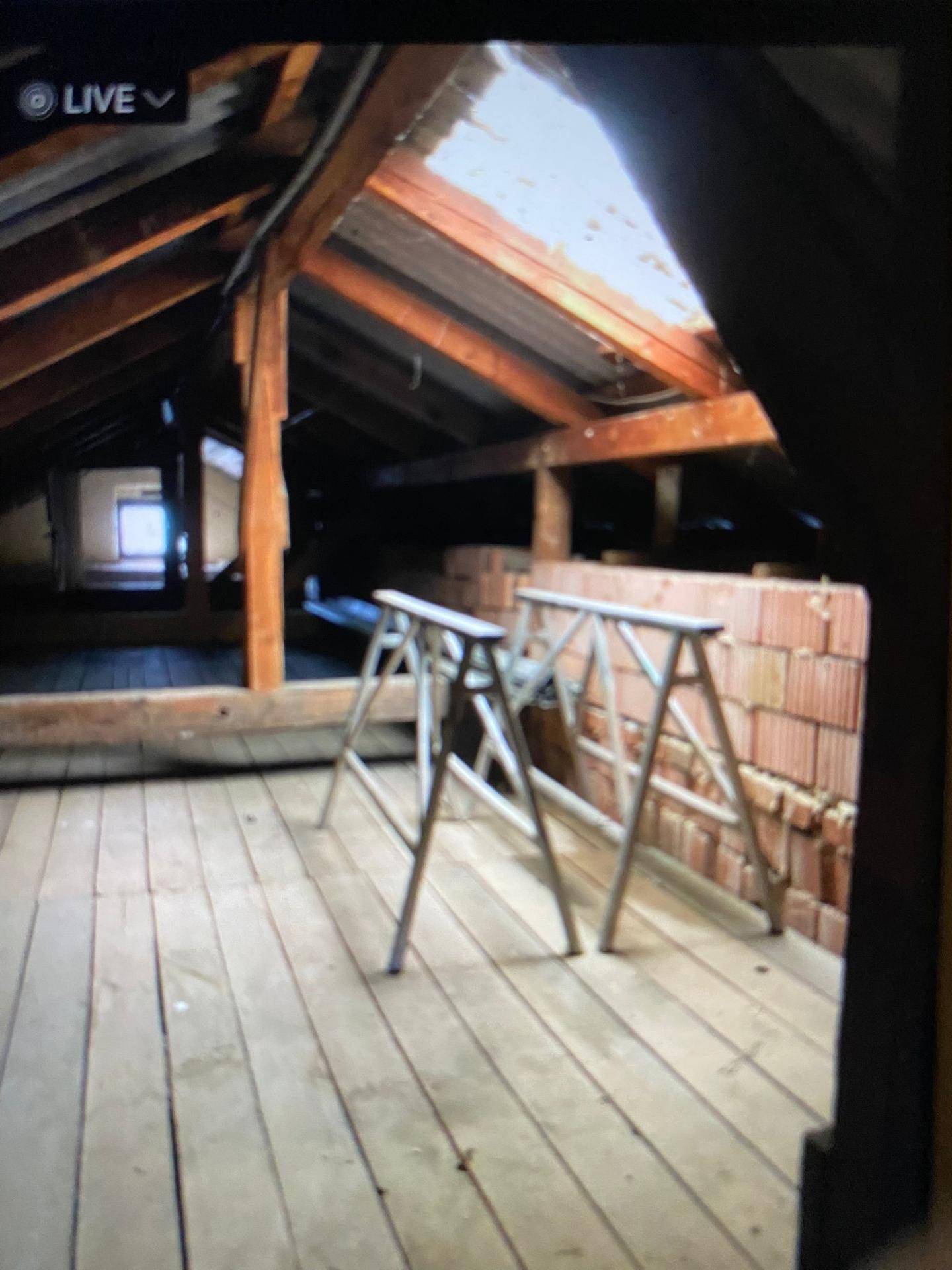 Unausgebauter Dachboden mit sichtbaren Holzbalken, Holzfußboden und Dachfenster.