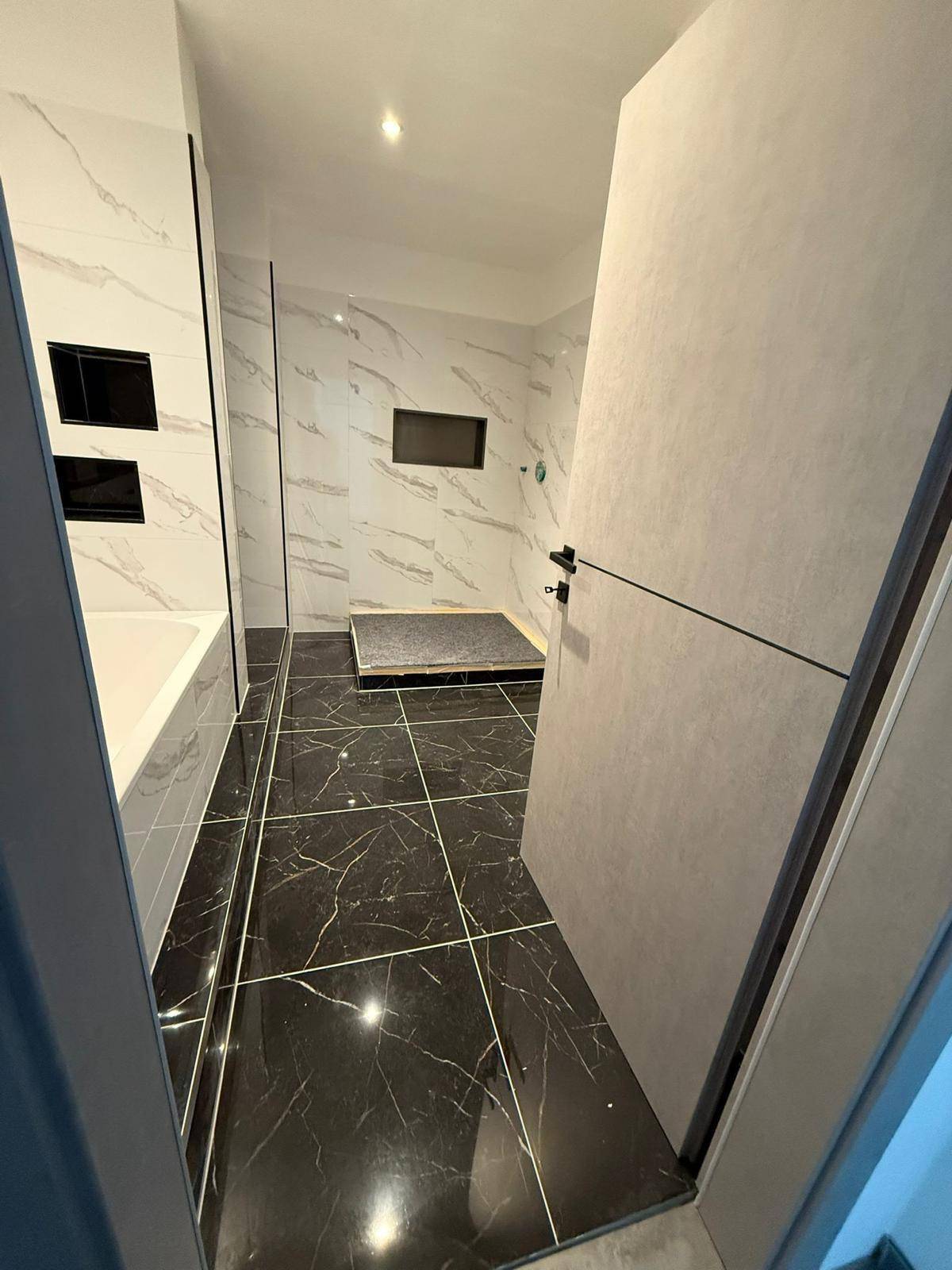 Elegantes Badezimmer mit einer ebenerdigen Dusche und kontrastierenden schwarz-weißen Marmorfliesen.