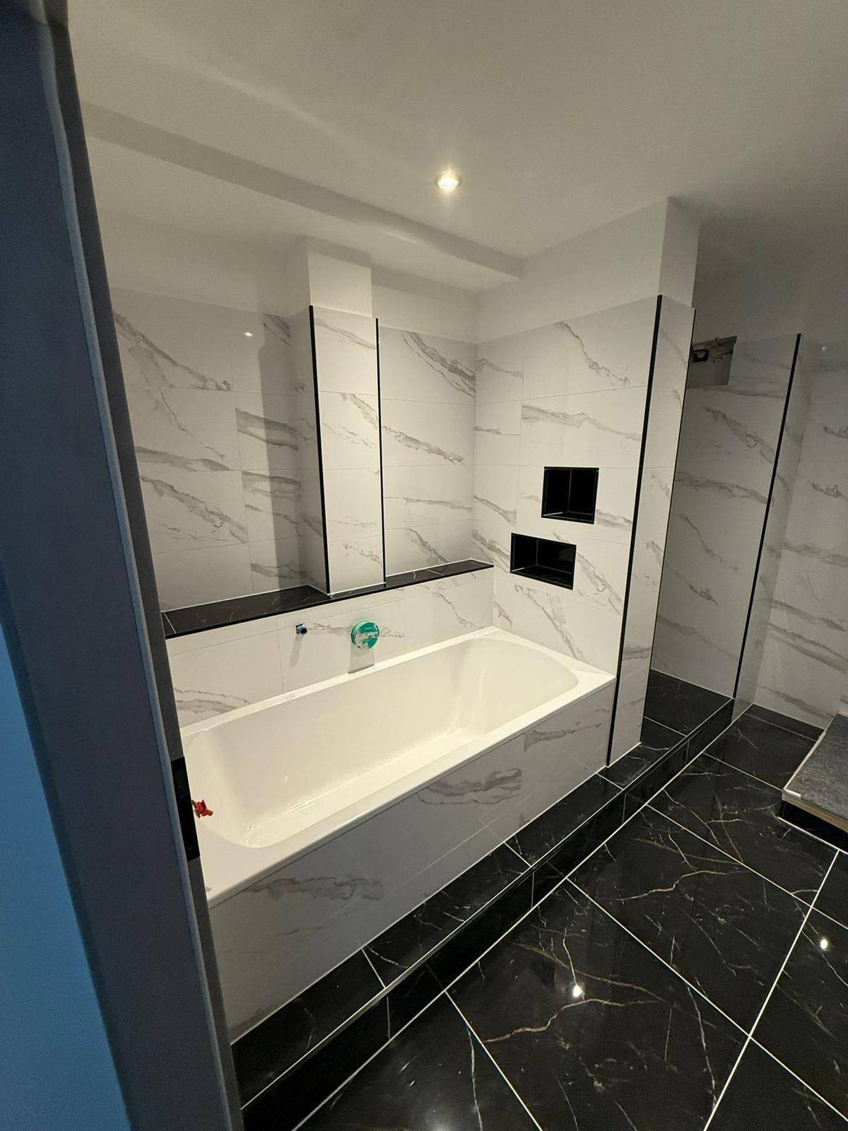 Modernes Badezimmer mit eingebauter Badewanne und eleganten schwarz-weißen Marmorfliesen an Wänden und Boden.