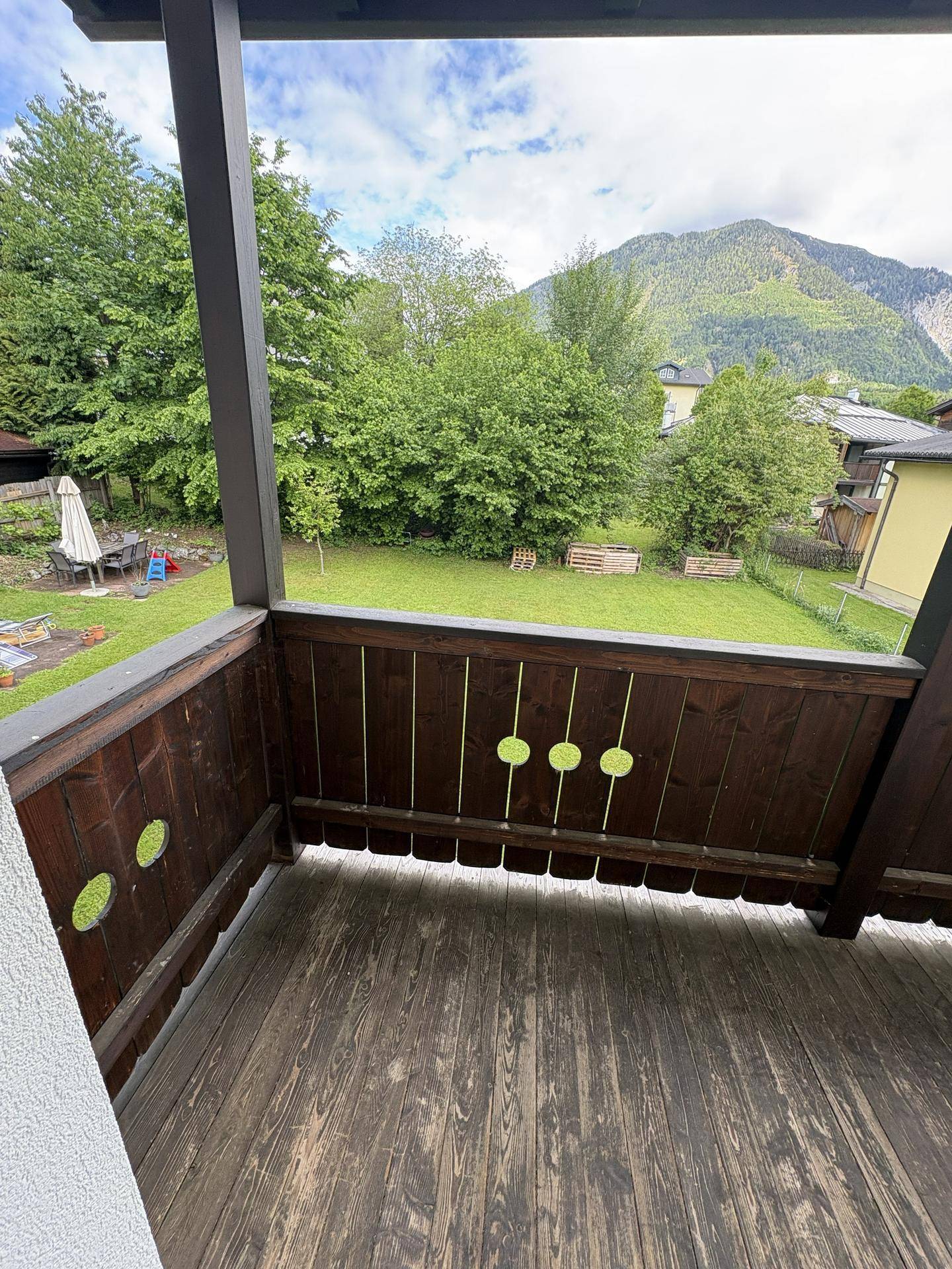 Holzbalkon mit Blick auf den grünen Garten und die umliegenden Berge.
