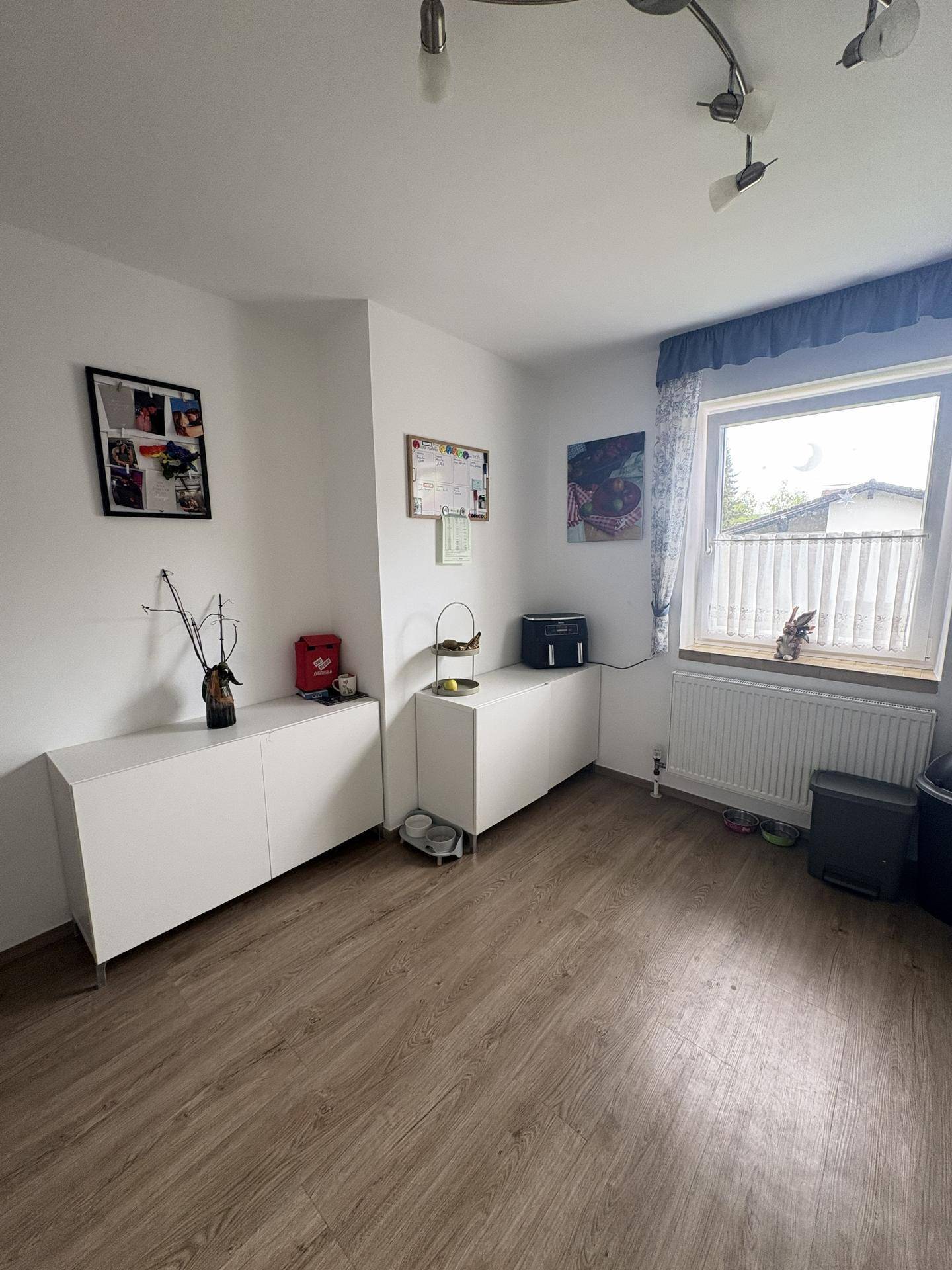 Gemütliches Zimmer mit Laminatboden, weißen Schränken und einem Fenster mit Blick ins Grüne.
