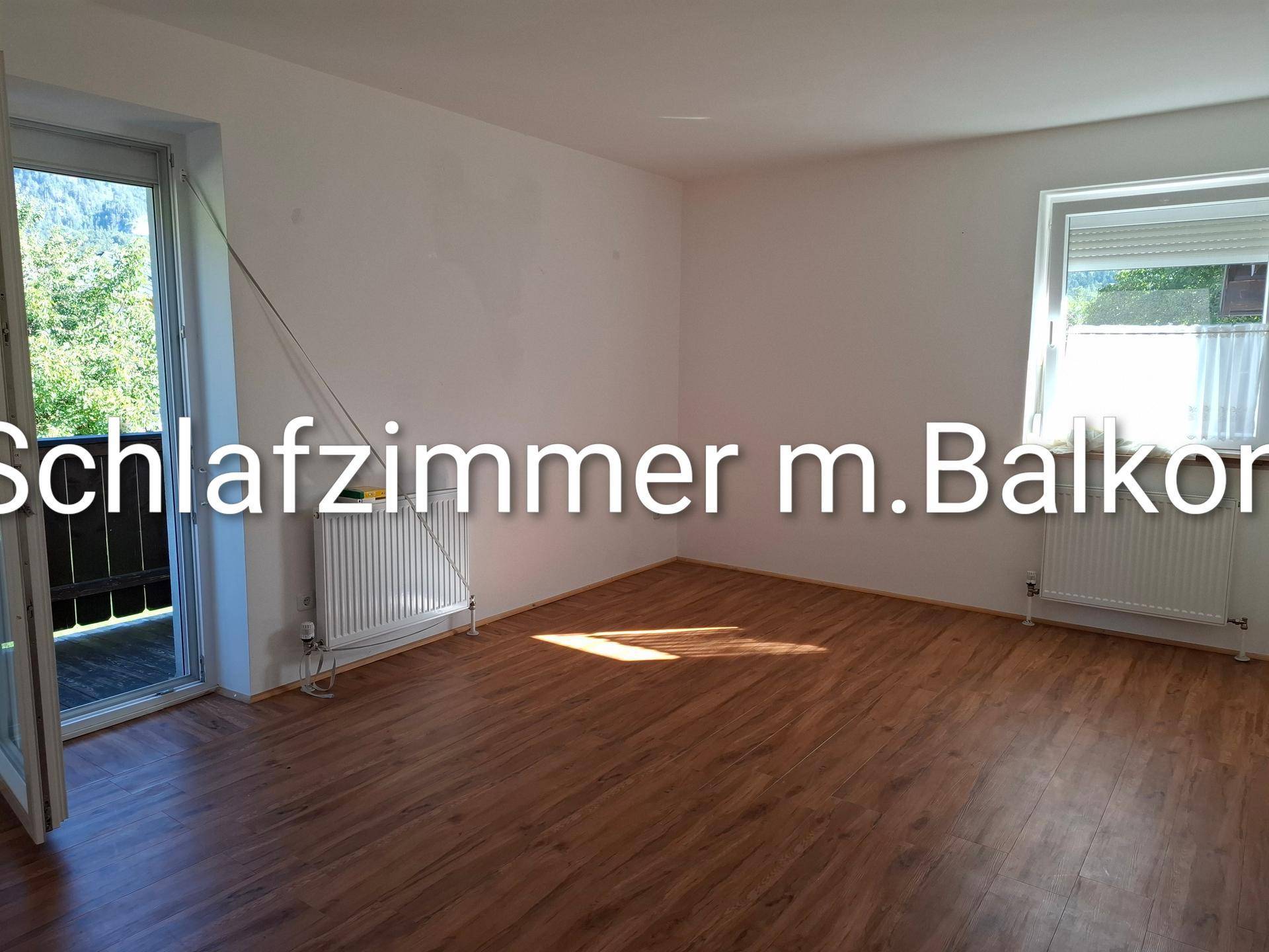 Geräumiges Schlafzimmer mit Holzboden und direktem Zugang zum Balkon, umgeben von Natur.