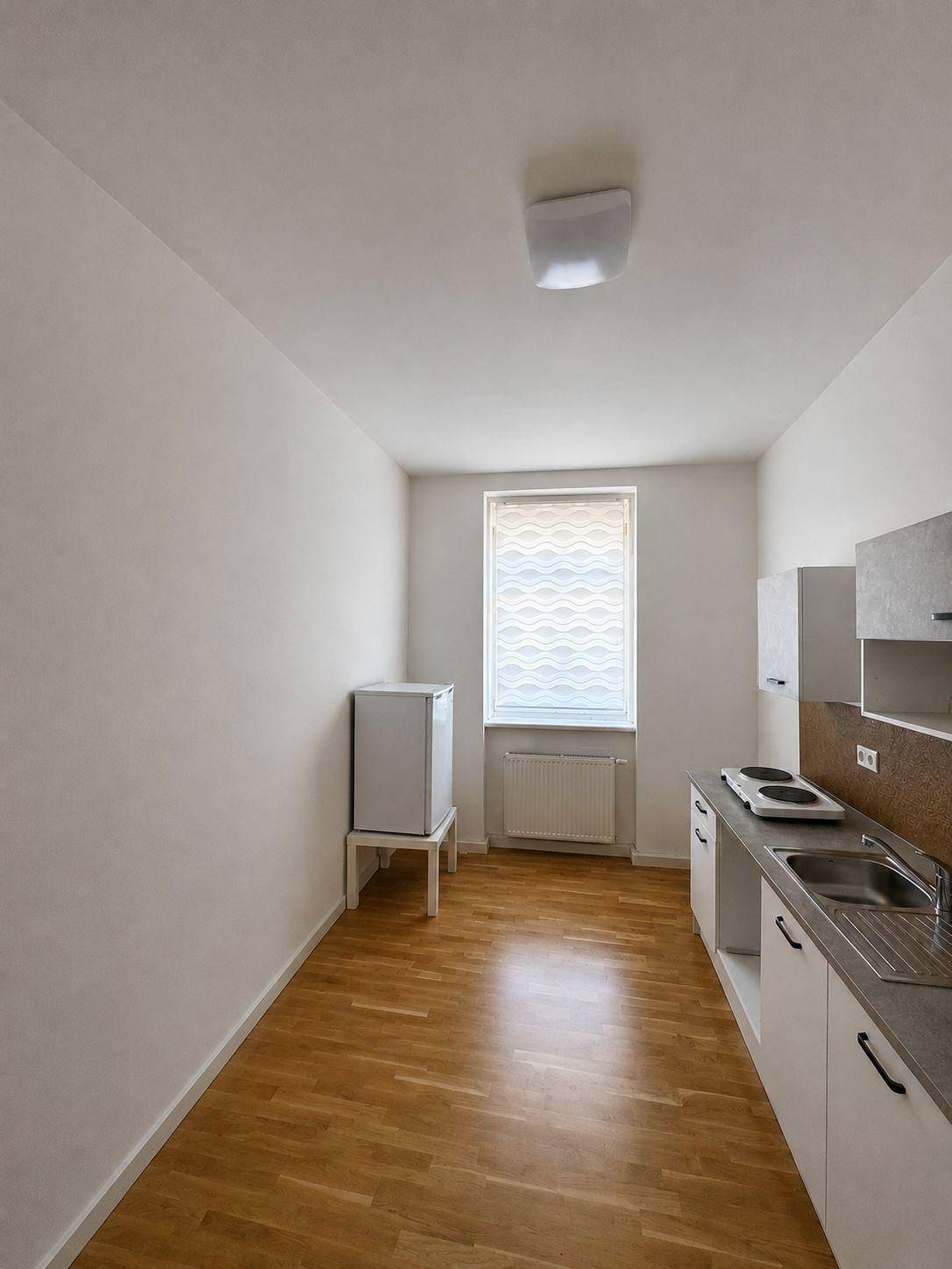 Helle Küchenzeile mit Holzboden, Fenster und minimalistischen Schränken.