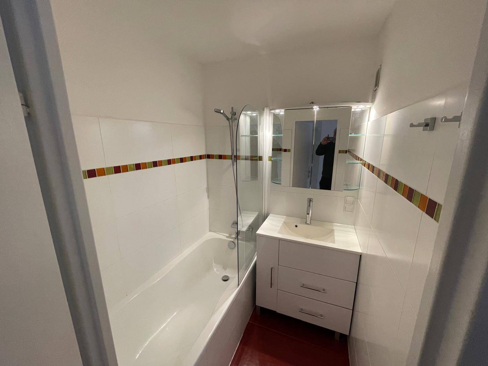 Modernes Badezimmer mit Badewanne, Duschabtrennung, Einzelwaschbecken und Spiegelschrank, hell gefliest.