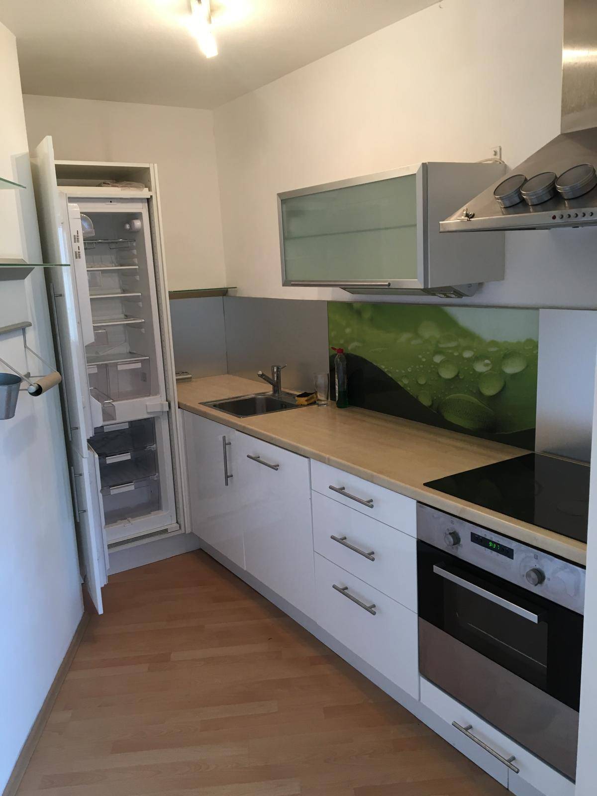 Funktionale Einbauküche mit weißen Schränken, Holz-Arbeitsplatte und modernen Geräten, inklusive Kühlschrank.