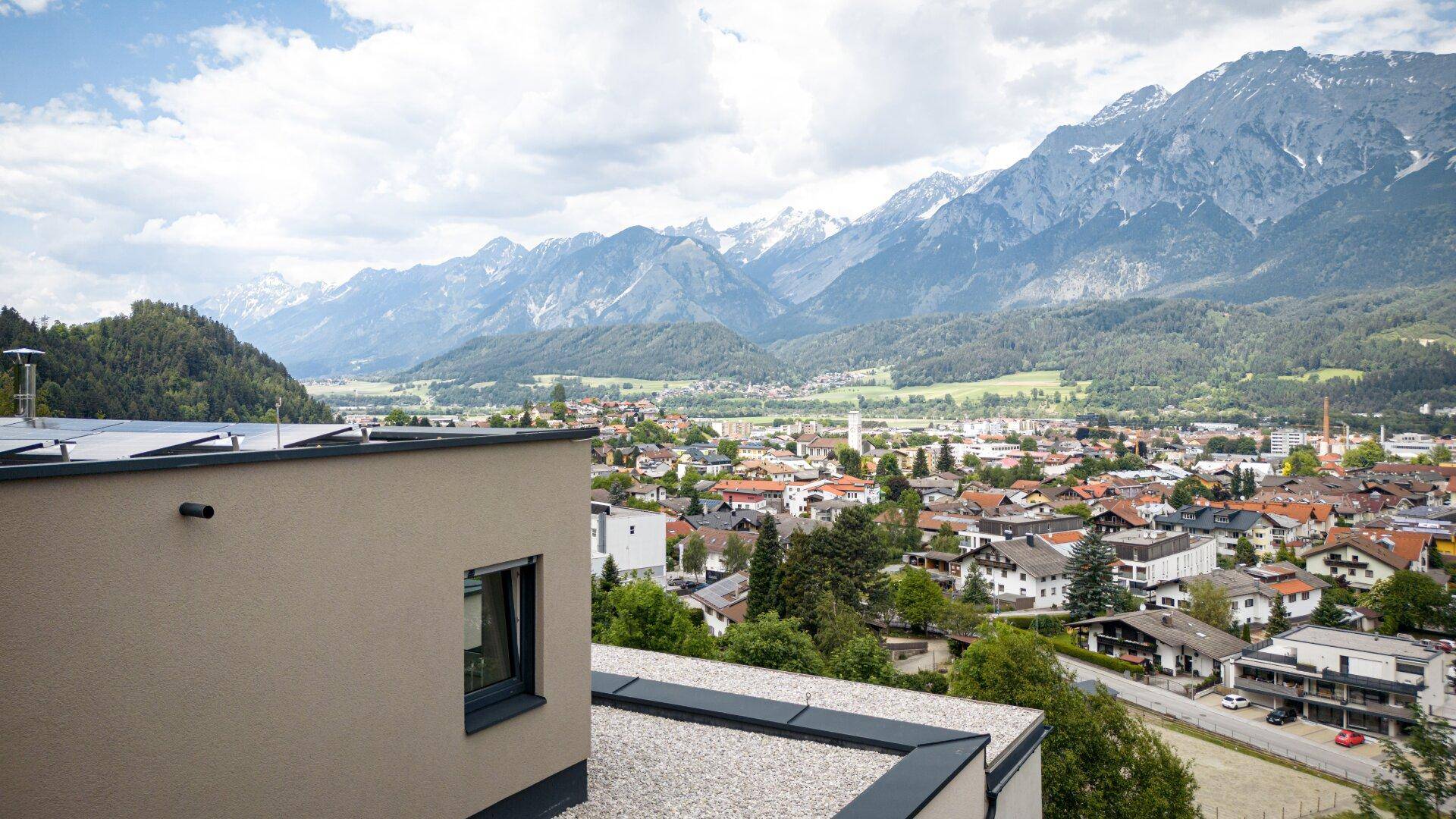 Flachdach eines modernen Gebäudes mit weitem Blick über eine Stadt und die umliegende Berglandschaft.