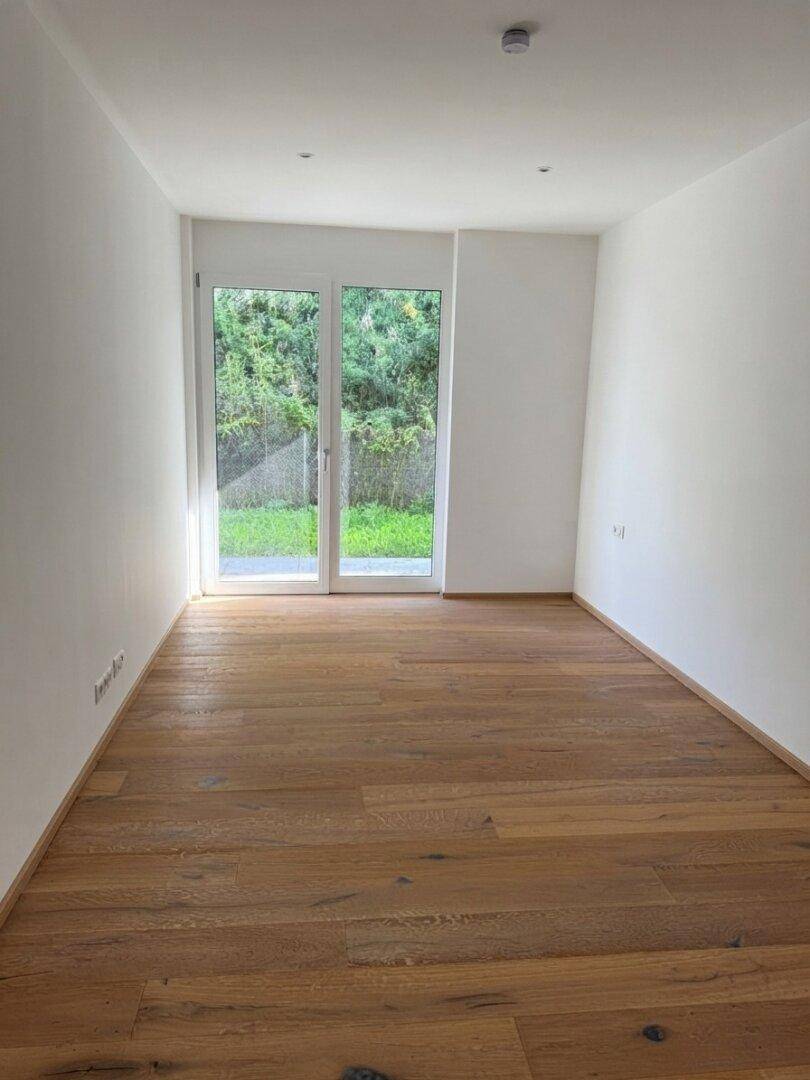 Helles Zimmer mit Eichenparkettboden und direktem Zugang zu einem grünen Außenbereich.