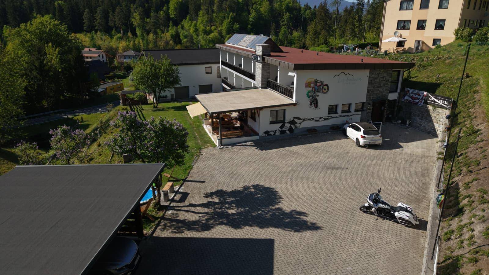 Luftaufnahme des Hauptgebäudes mit Parkplatz, Auto, Motorrad und einem Carport.
