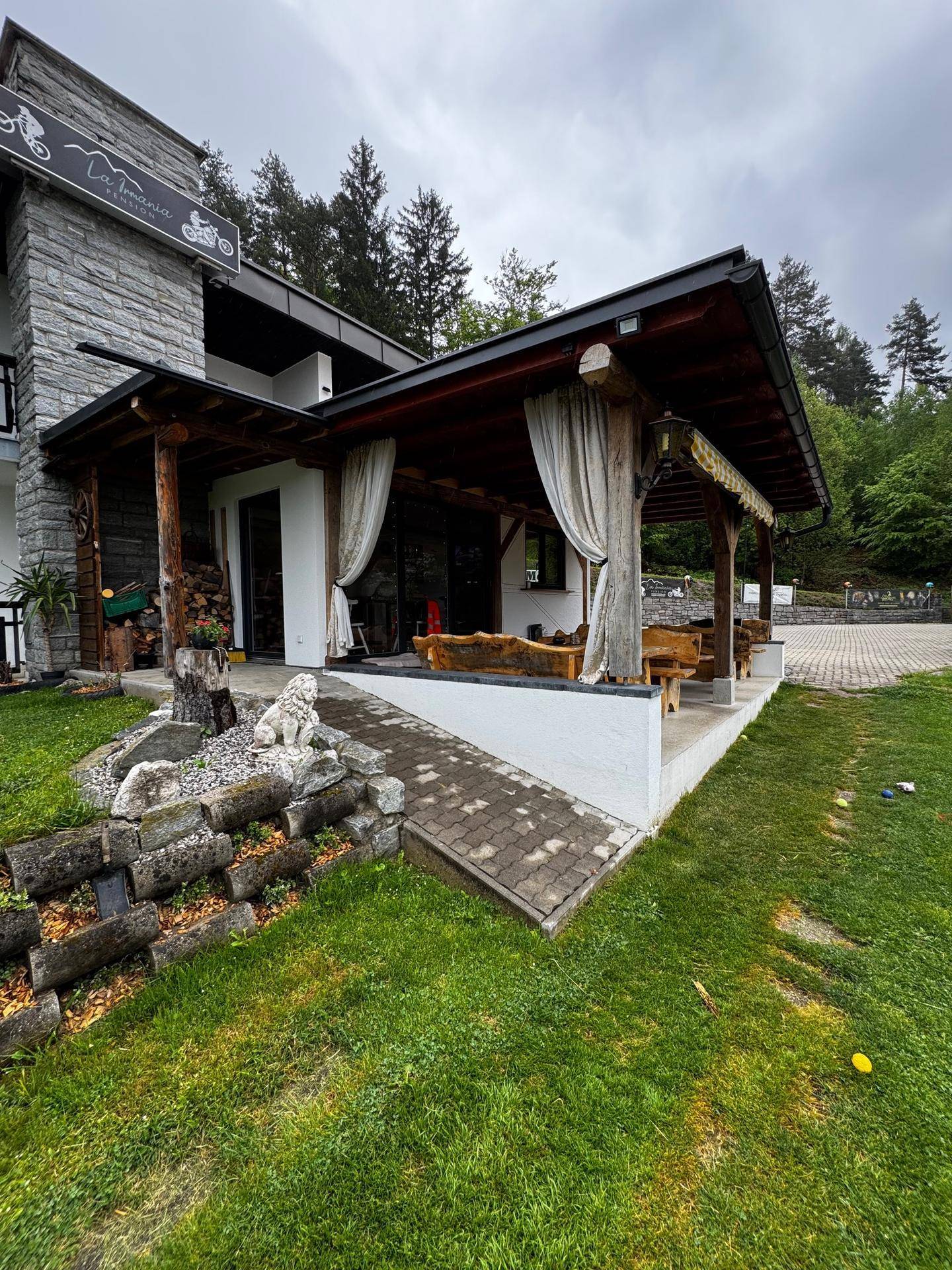 Überdachte Terrasse mit rustikalen Holzmöbeln, Steinmauer und einer Rampe für barrierefreien Zugang.