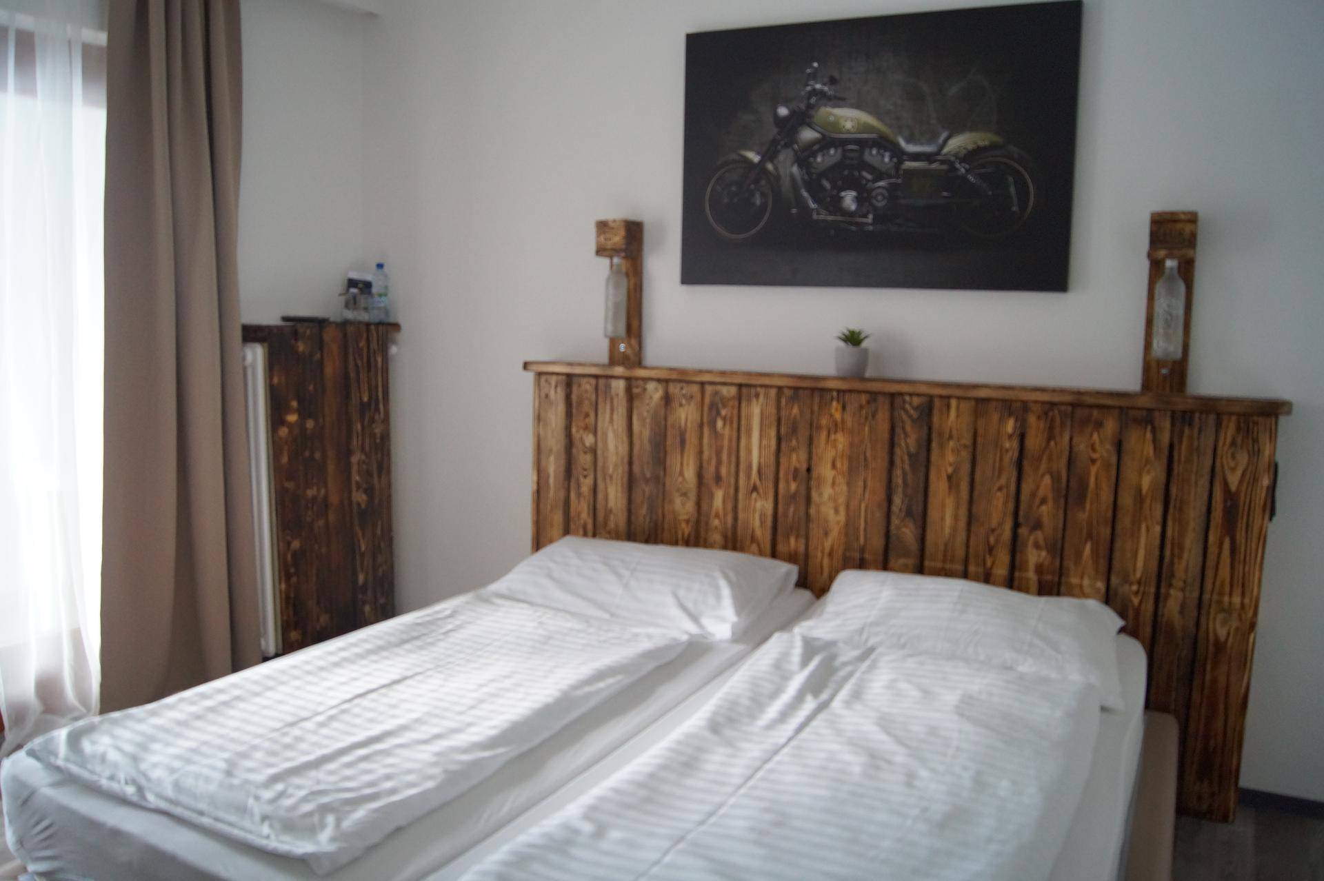 Gemütliches Schlafzimmer mit rustikalem Holz-Kopfteil, weißer Bettwäsche und einem Motorradbild an der Wand.