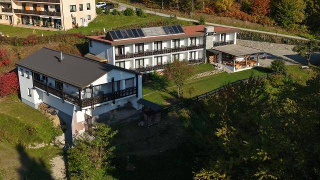 Luftaufnahme von mehreren Gebäuden in einer grünen Landschaft mit Solarpaneelen auf einem Dach.