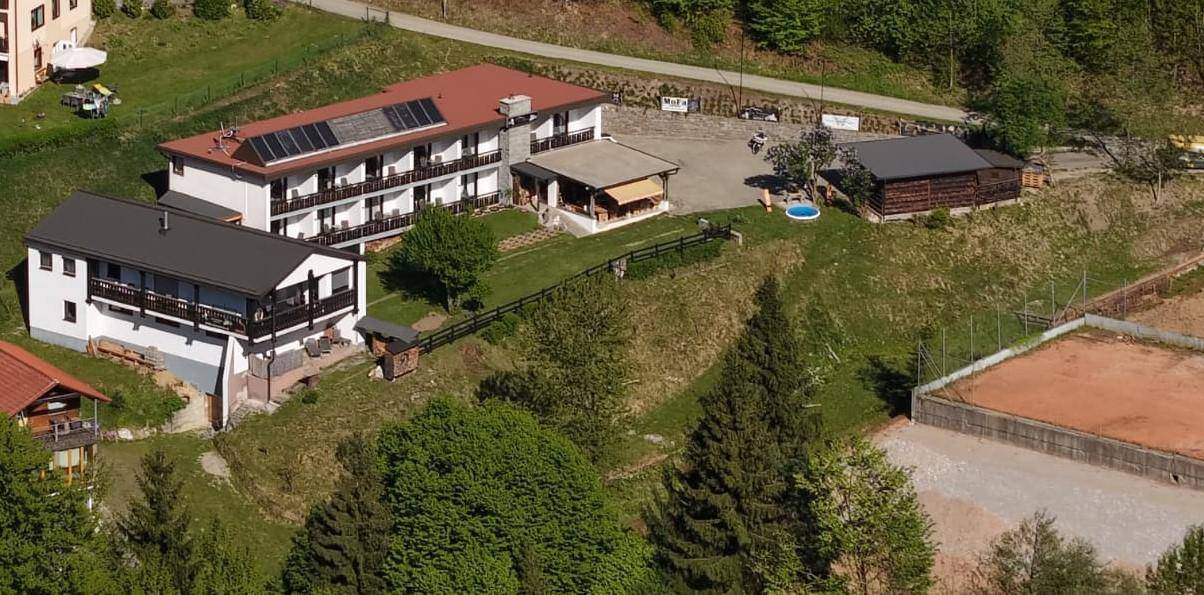 Luftaufnahme von mehreren Gebäuden in einer grünen Landschaft mit Solarpaneelen und einem Tennisplatz.
