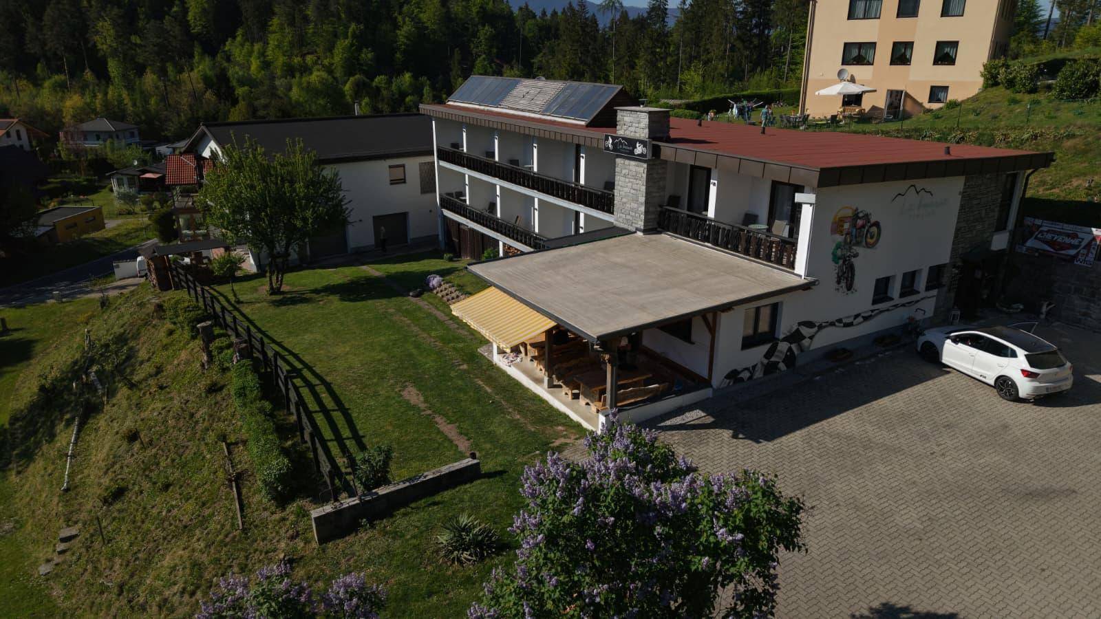 Luftaufnahme des Hauptgebäudes mit Parkplatz, Grünfläche und umliegender Natur, inklusive Solarpaneelen.
