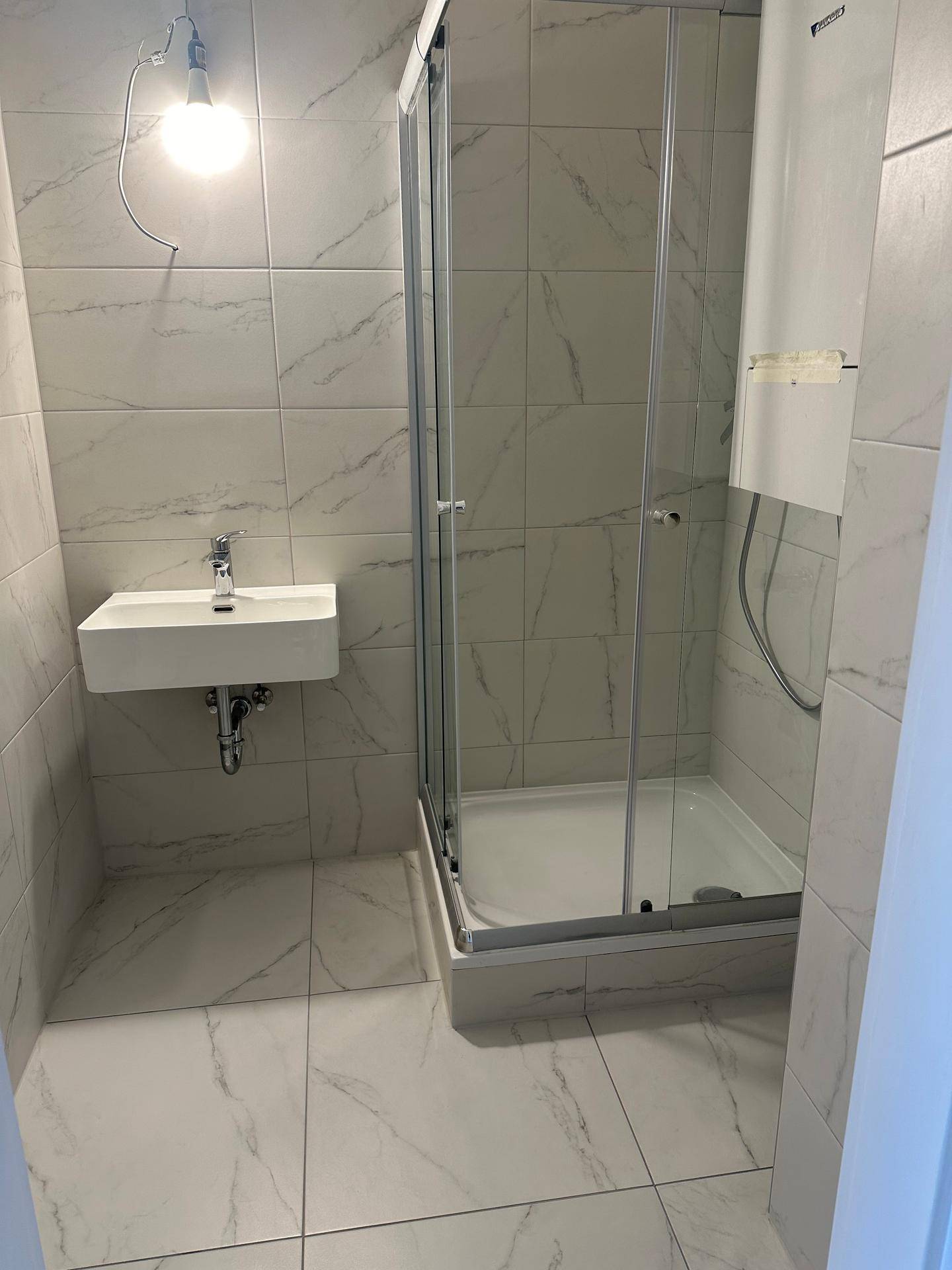 Modernes Badezimmer mit Duschkabine, Einzelwaschbecken und hellen Marmorfliesen.