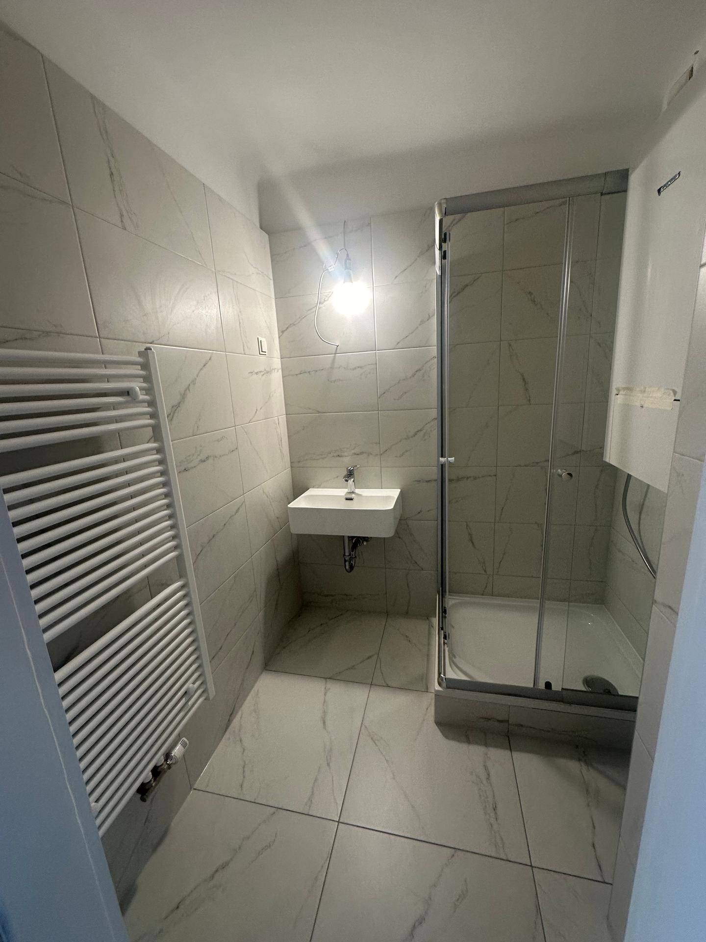 Helles Badezimmer mit Duschkabine, Einzelwaschbecken und beheiztem Handtuchhalter.