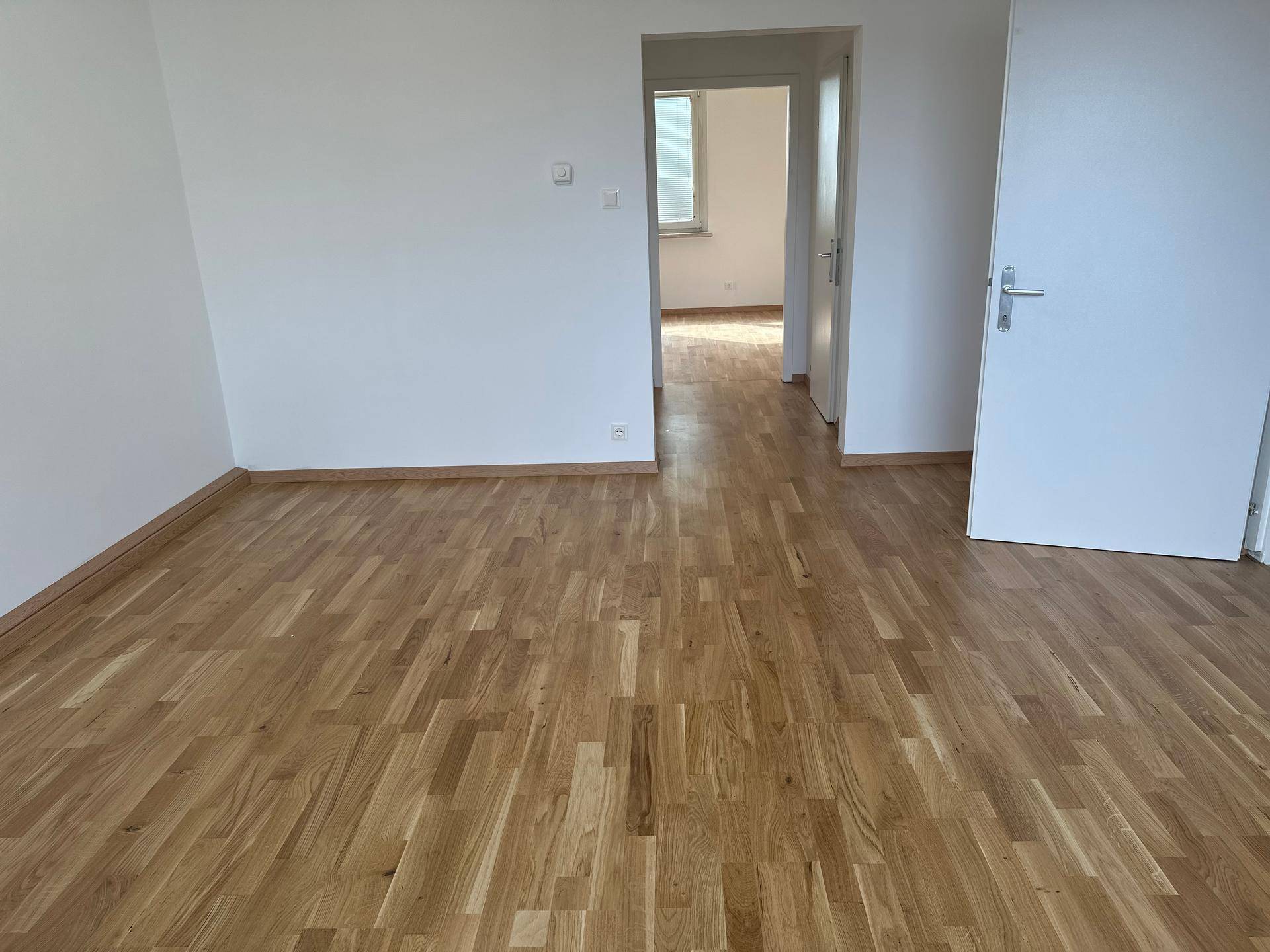 Geräumiger, leerer Raum mit hellem Holzparkett und weiß gestrichenen Wänden.