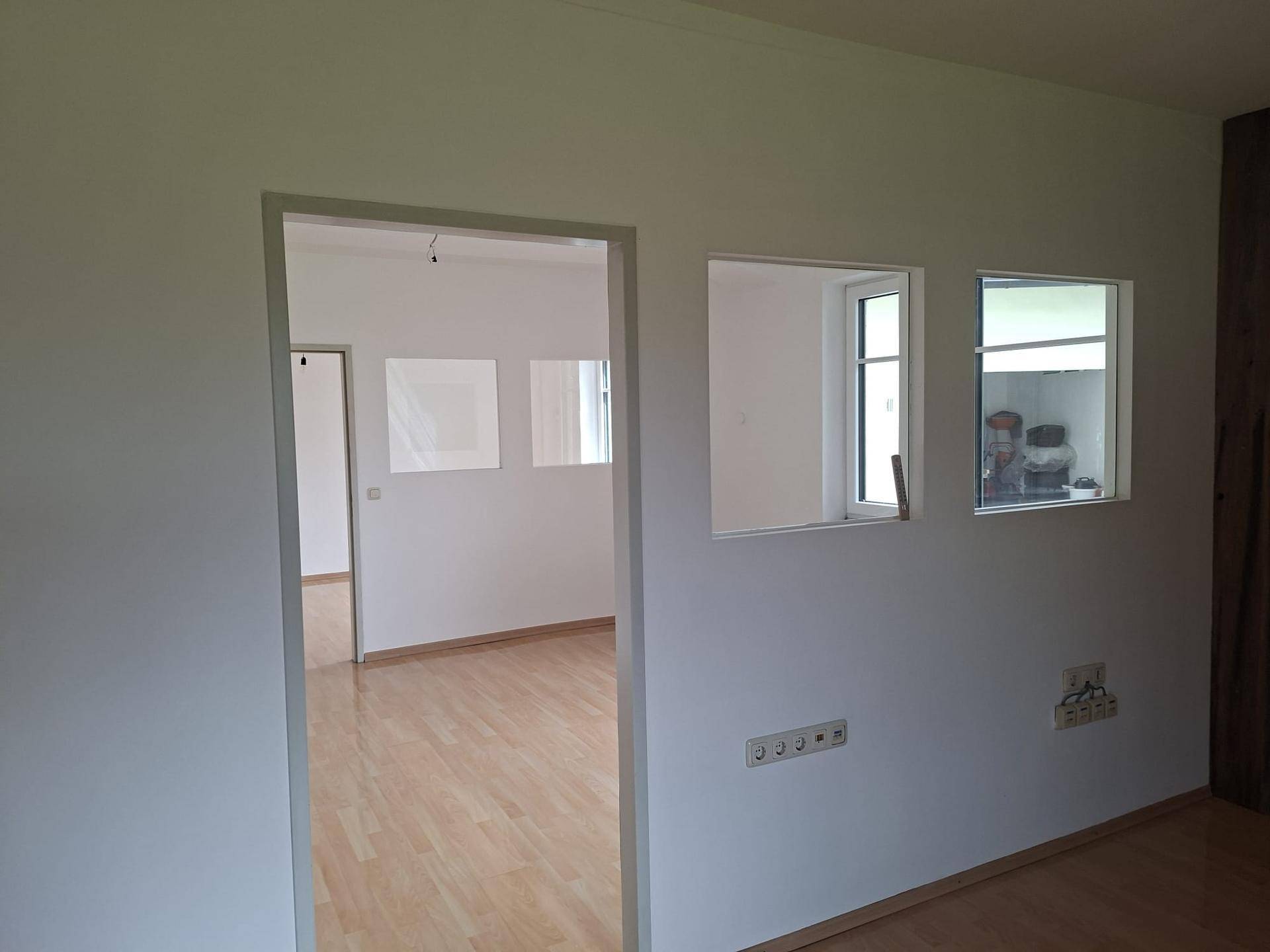 Heller Flur mit Durchgang zu einem weiteren Raum und zwei kleinen Fenstern an der Wand.