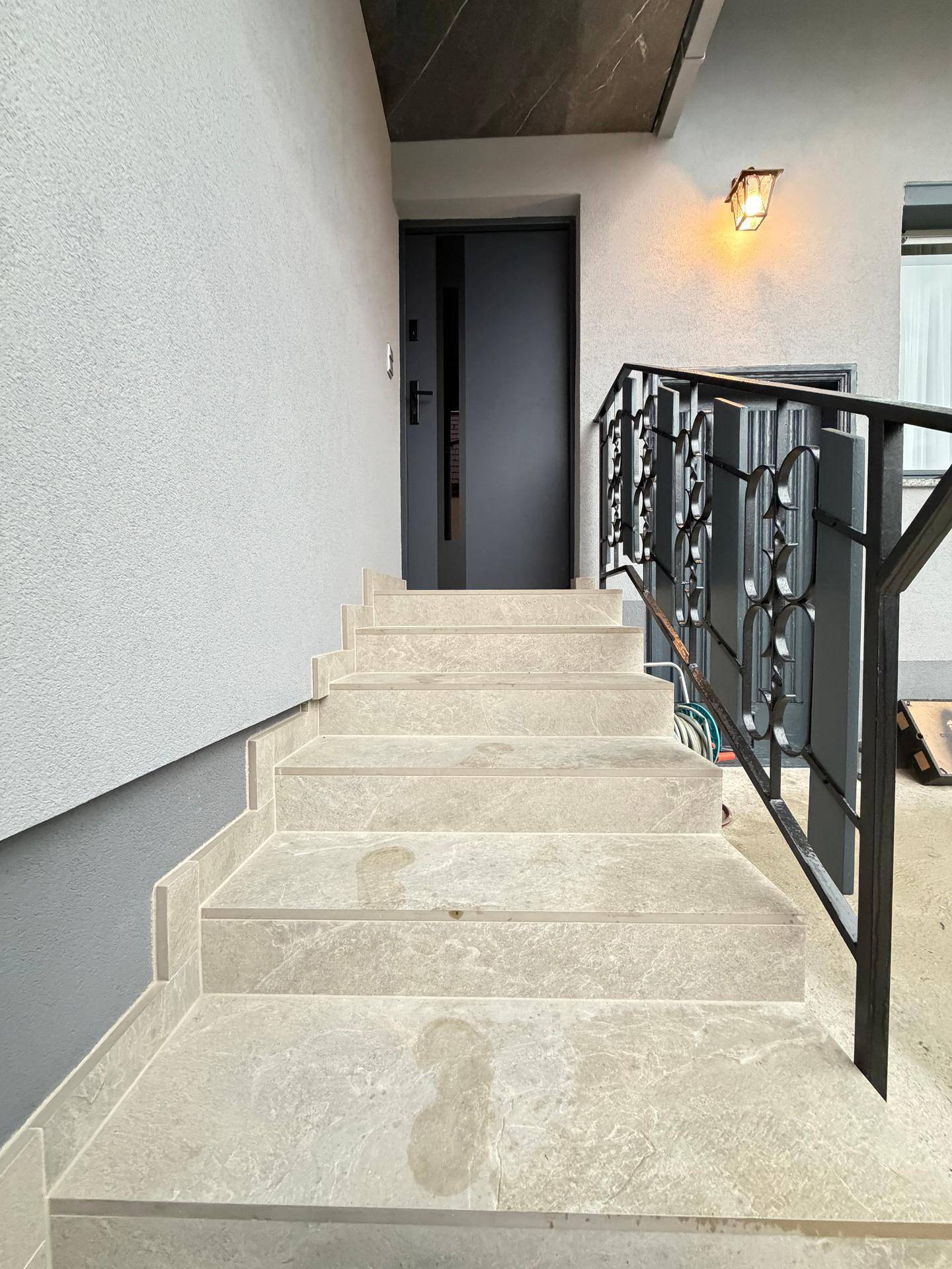 Steintreppe mit schmiedeeisernem Geländer führt zum Hauseingang.