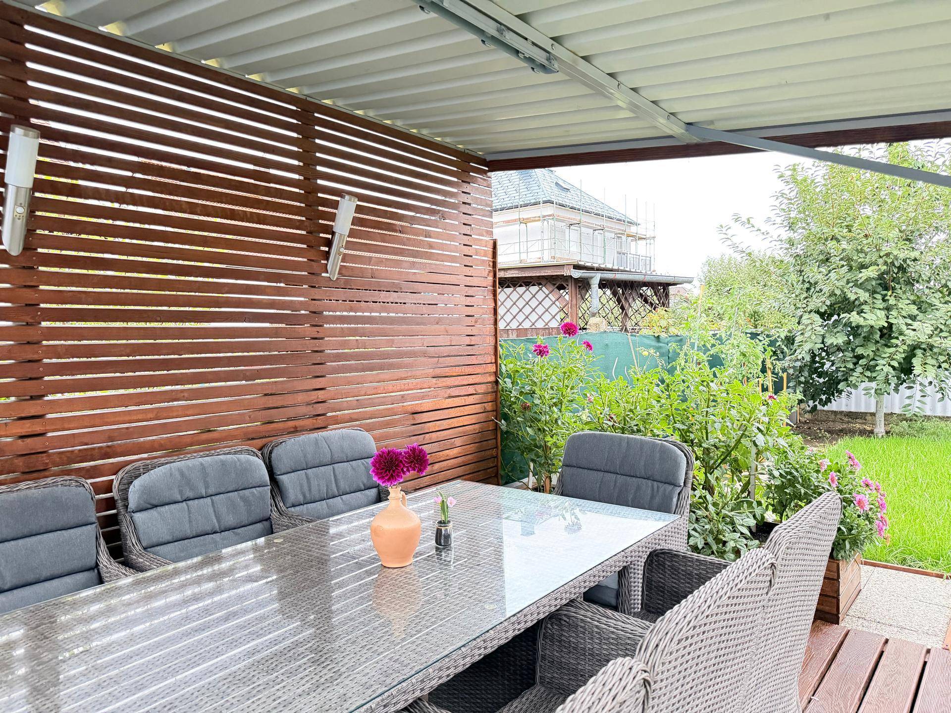 Gemütlicher überdachter Sitzbereich mit Korbmöbeln und Holzwand, ideal für entspannte Stunden im Freien.