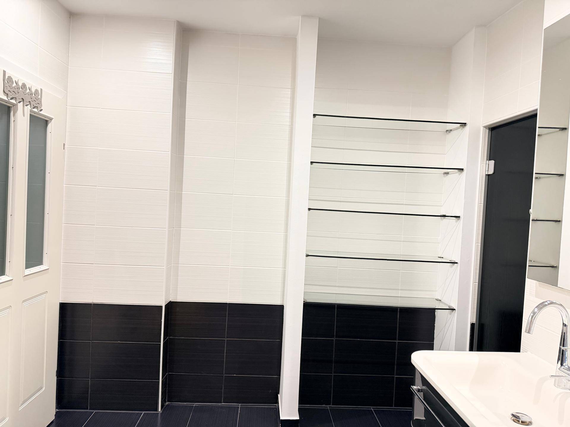 Badezimmer mit schwarzen und weißen Fliesen, Glasregalen und einem Waschbeckenbereich.