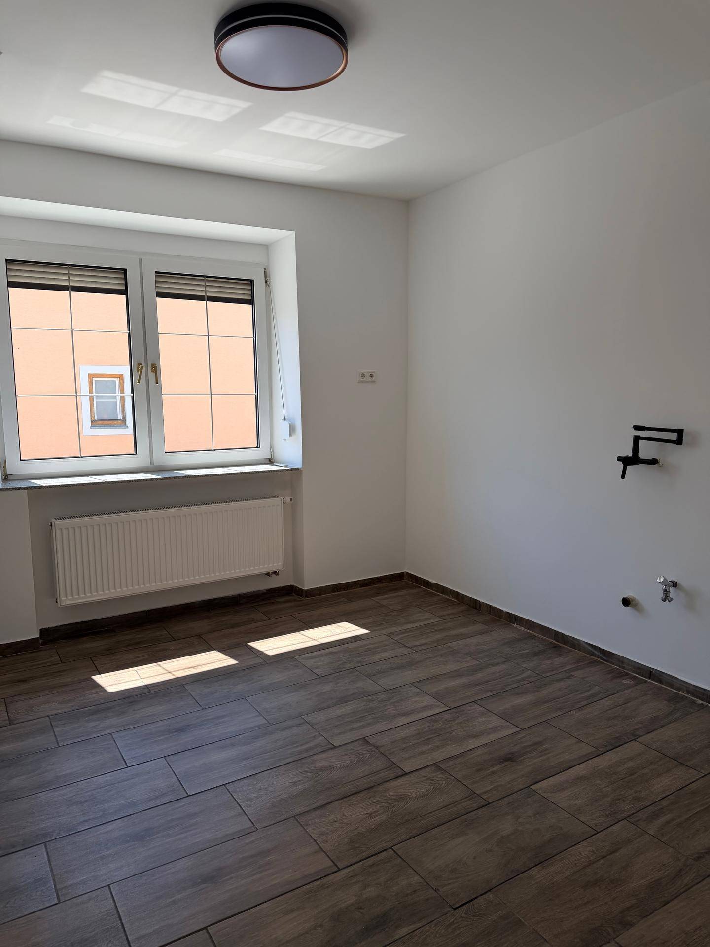 Helles Zimmer mit Fliesenboden und einem Fenster, das viel Tageslicht hereinlässt.