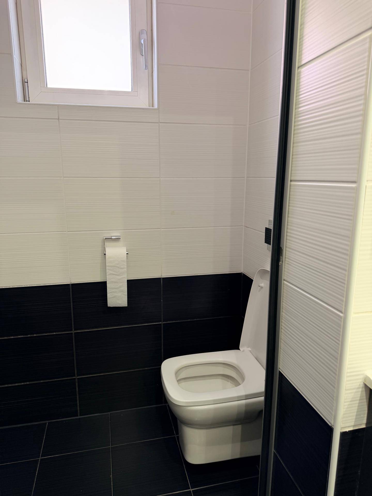 Separate Toilette mit Fenster, weißen und schwarzen Fliesen und Wand-WC.
