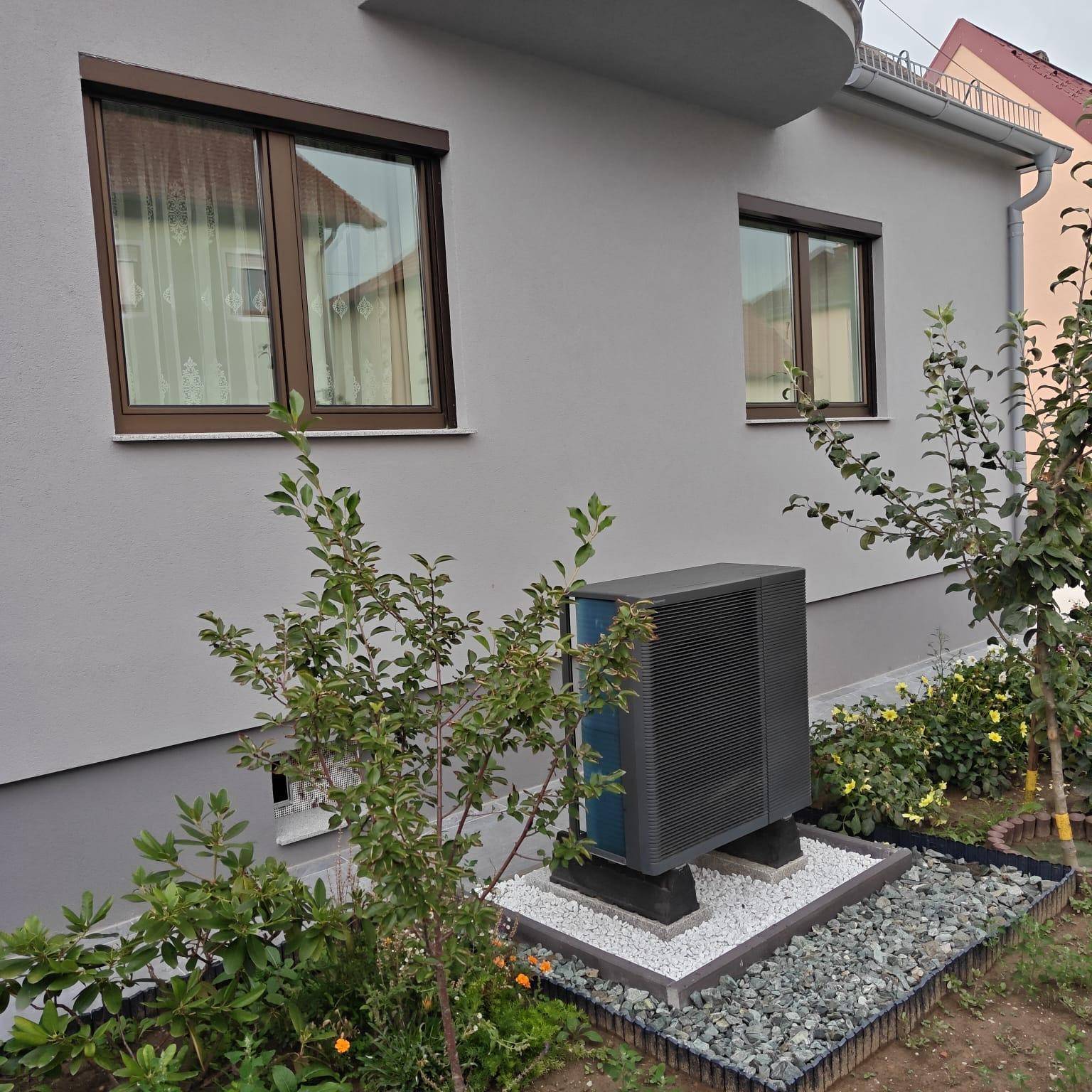 Wärmepumpe an der Seite des Hauses, umgeben von kleinen Pflanzen und Kies.