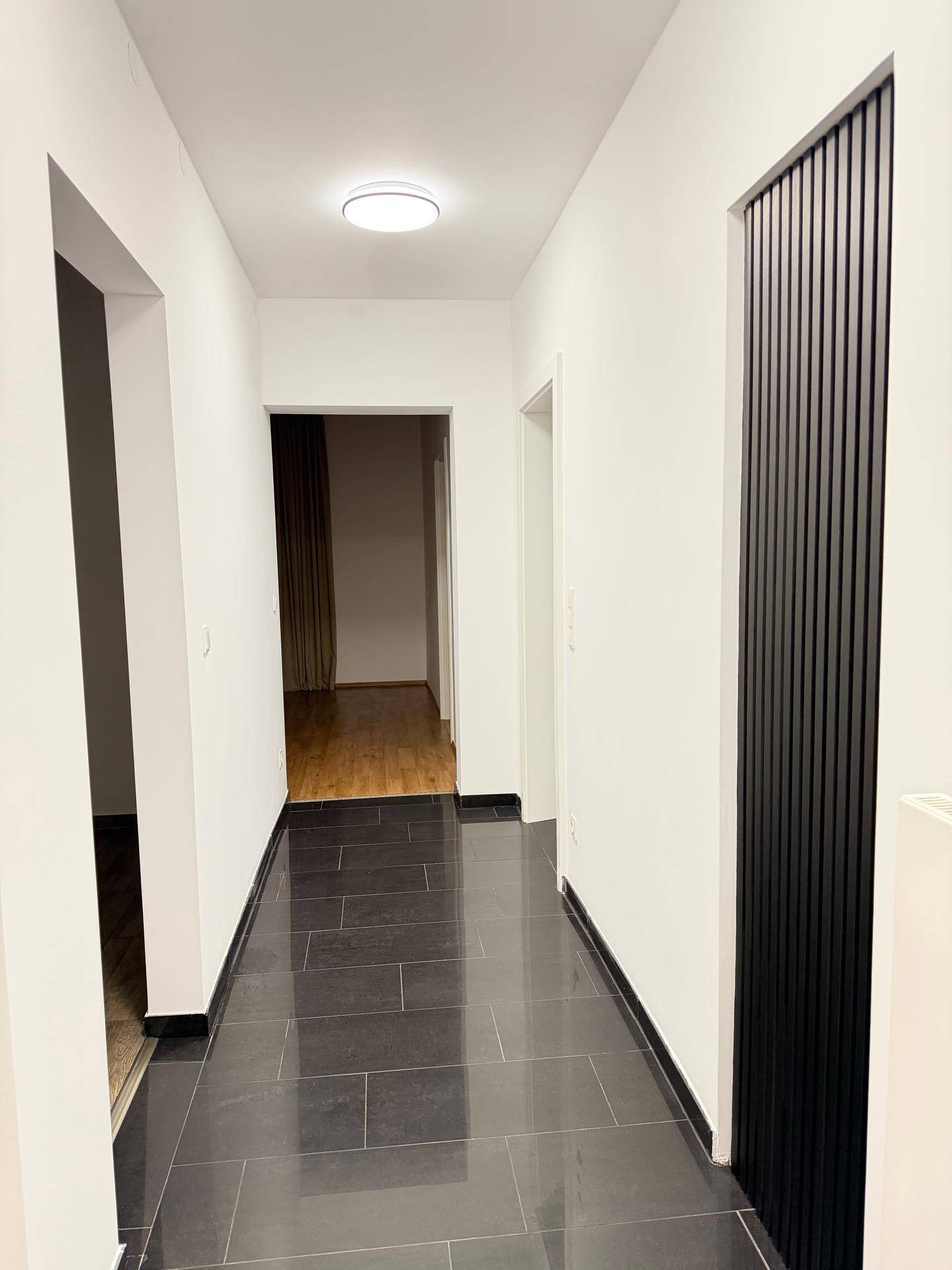 Moderner Flur mit dunklen Fliesen und einer vertikalen Holzverkleidung an der Wand.