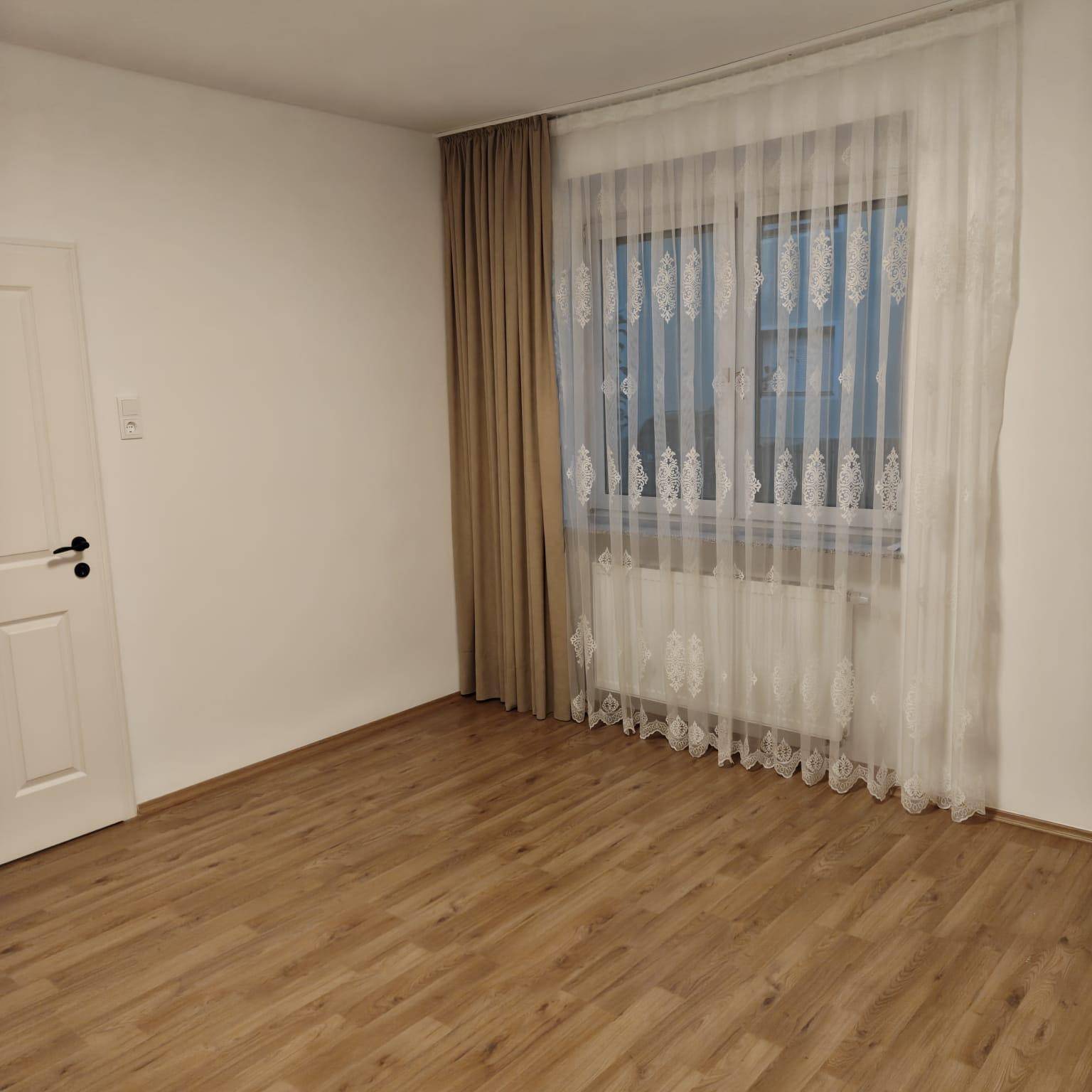 Helles Schlafzimmer mit Laminatboden und einem Fenster mit weißen Spitzenvorhängen.