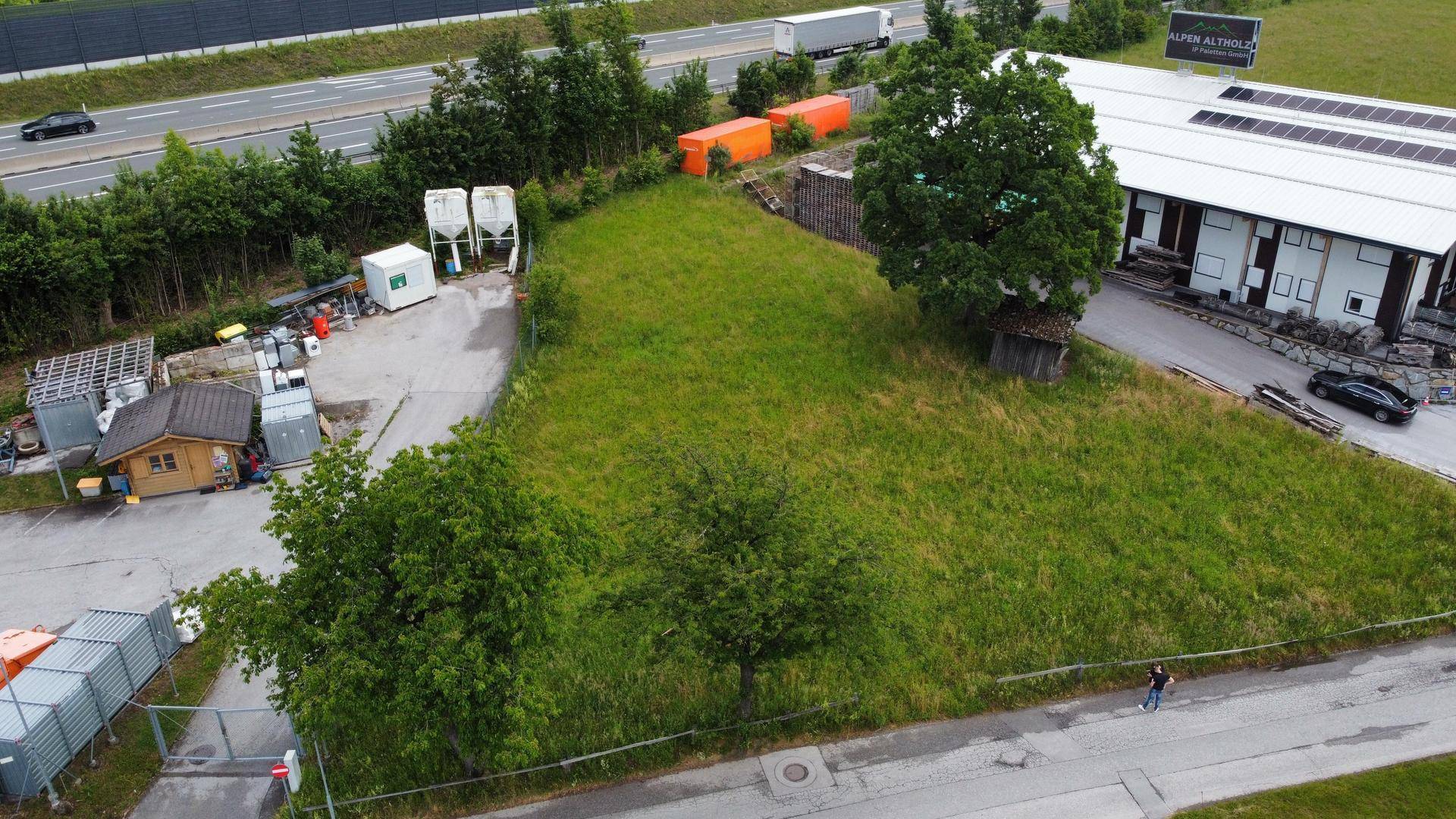 Luftaufnahme eines unbebauten Grundstücks neben einer Autobahn, umgeben von Bäumen und einigen Industriegebäuden.