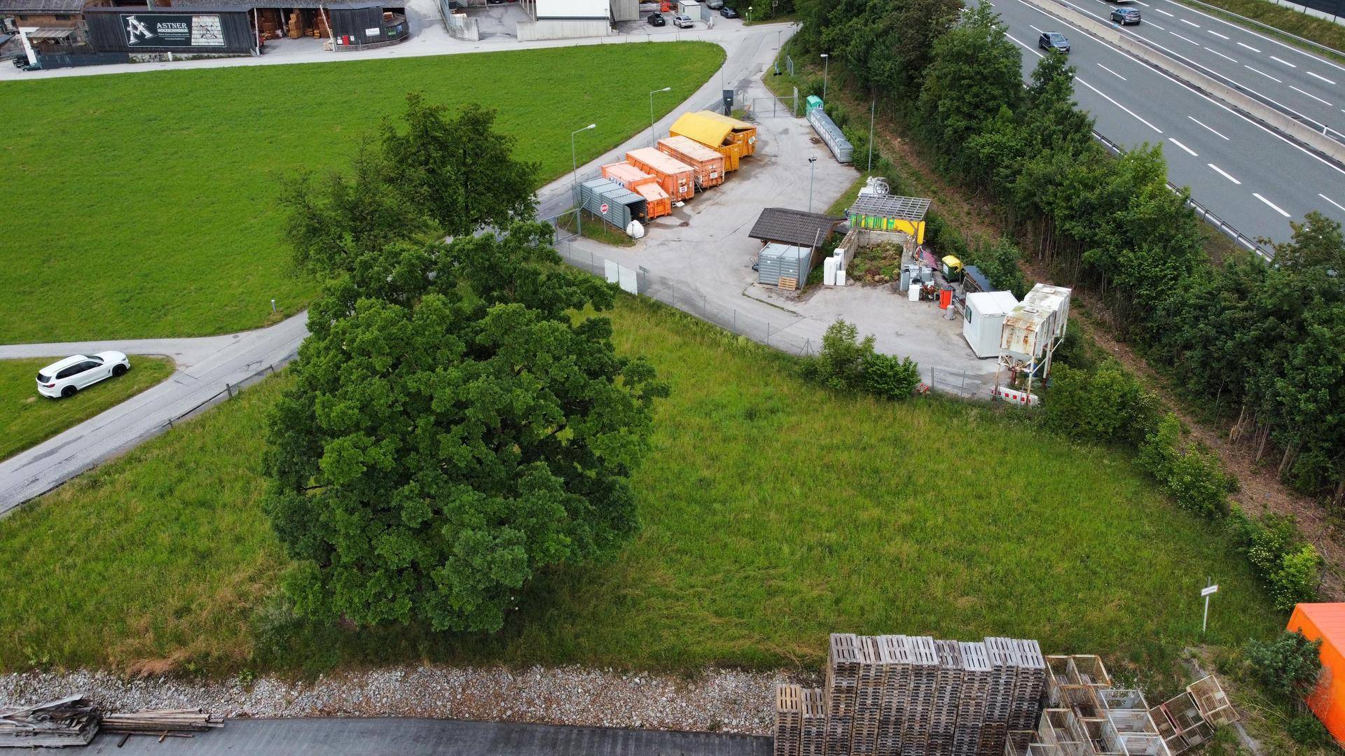 Luftaufnahme eines grünen Grundstücks mit einer Wertstoffsammelstelle und einer Autobahn im Hintergrund.