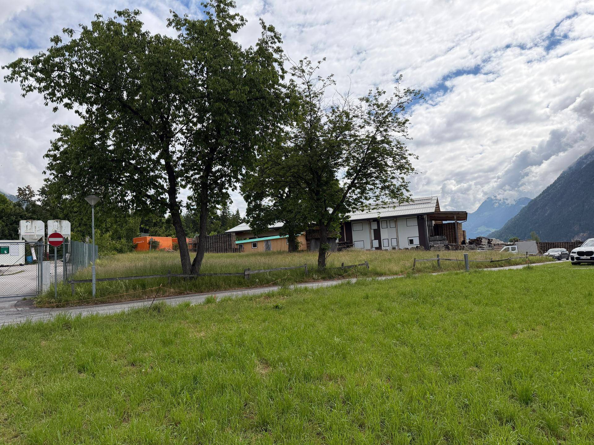 Weitläufiger Blick auf ein grünes Grundstück mit hohen Bäumen und einer beeindruckenden Bergkulisse im Hintergrund.