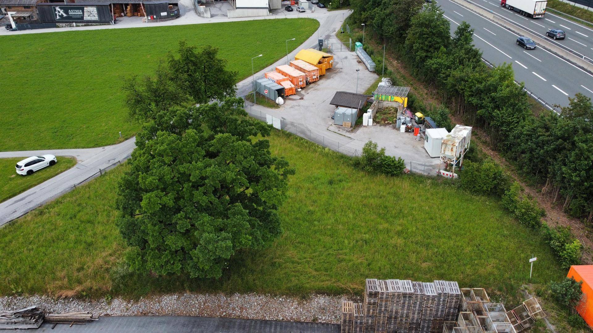 Luftaufnahme eines grünen Grundstücks mit einer Wertstoffsammelstelle und einer Autobahn im Hintergrund.
